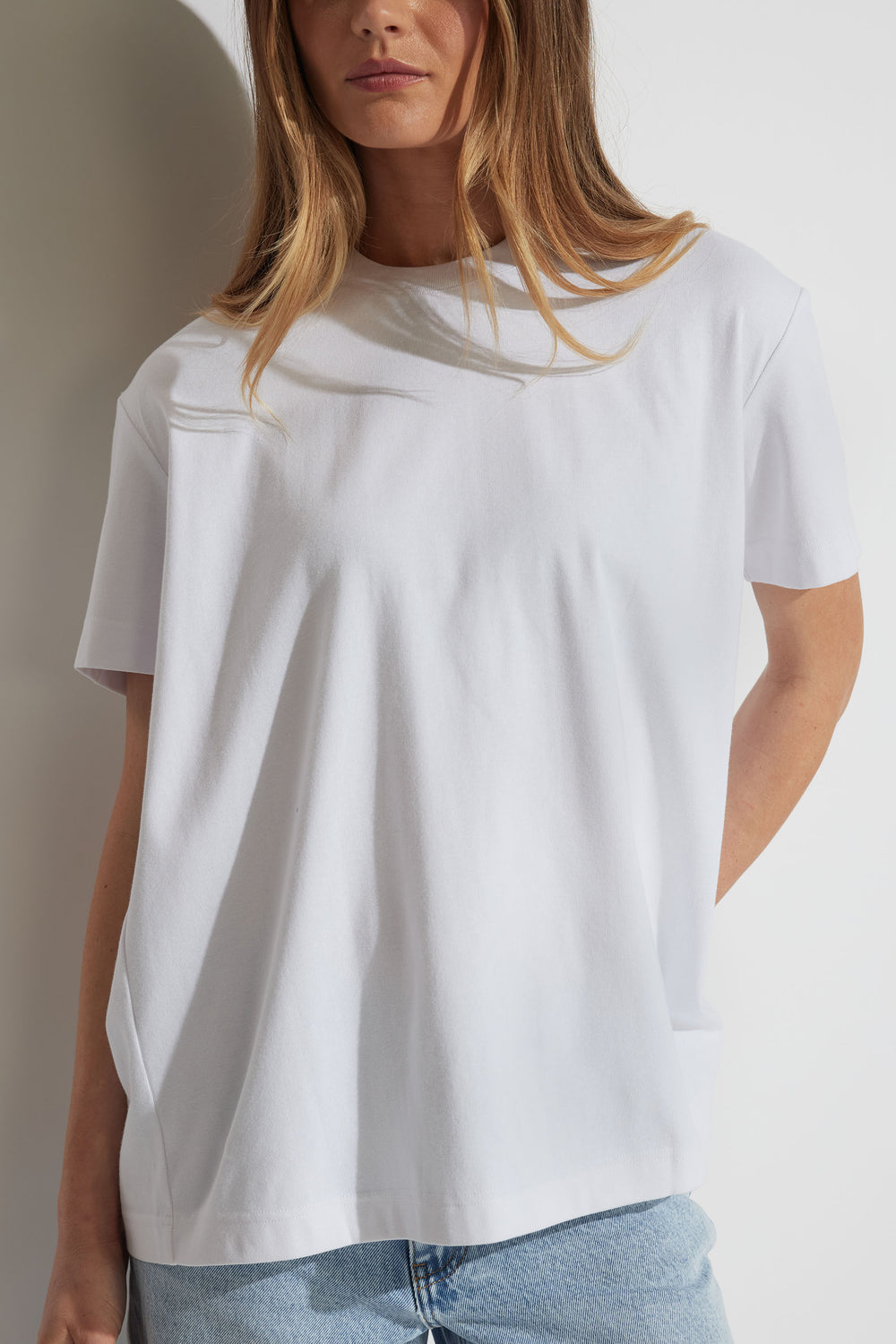 Woman wearing a relaxed white tee with metal detail and light blue denim jeans, styled for effortless everyday wear