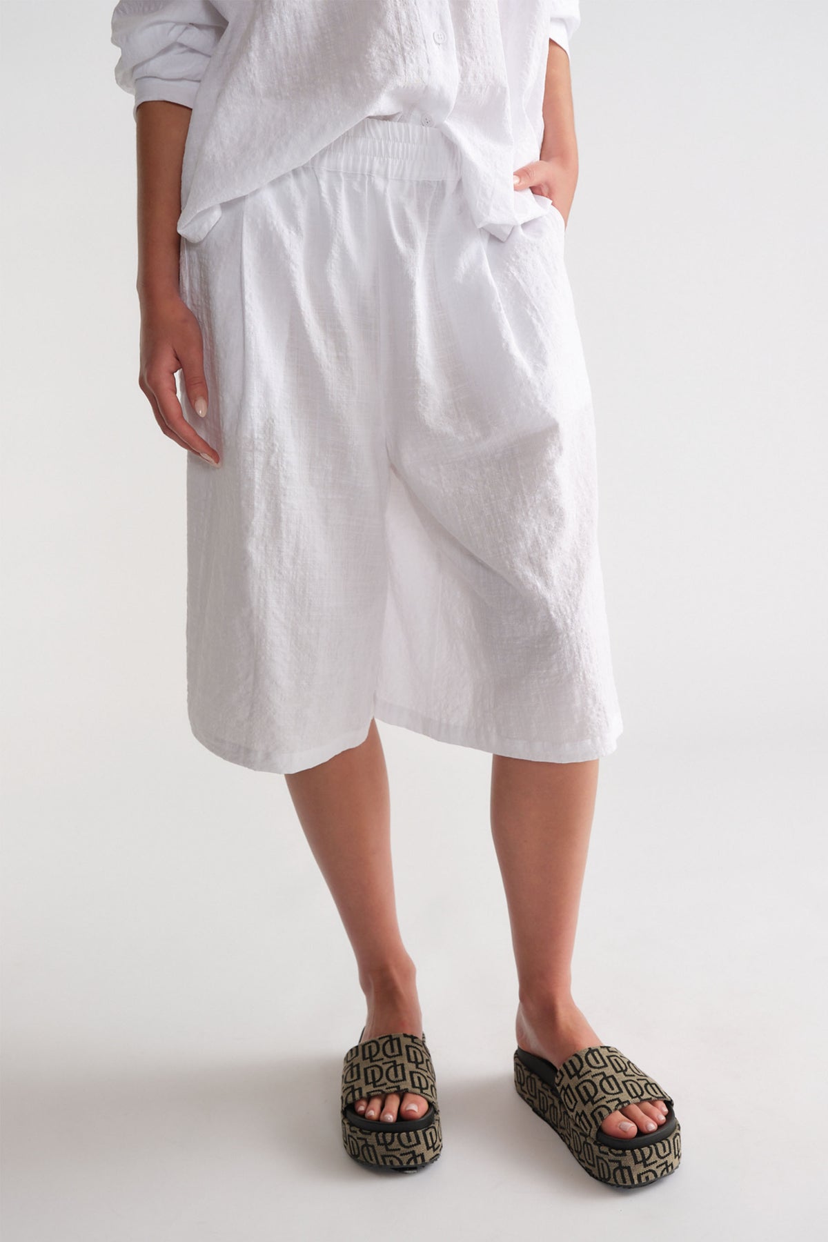 Woman wearing relaxed white Bermuda shorts paired with printed slip-on platform sandals and a loose white top