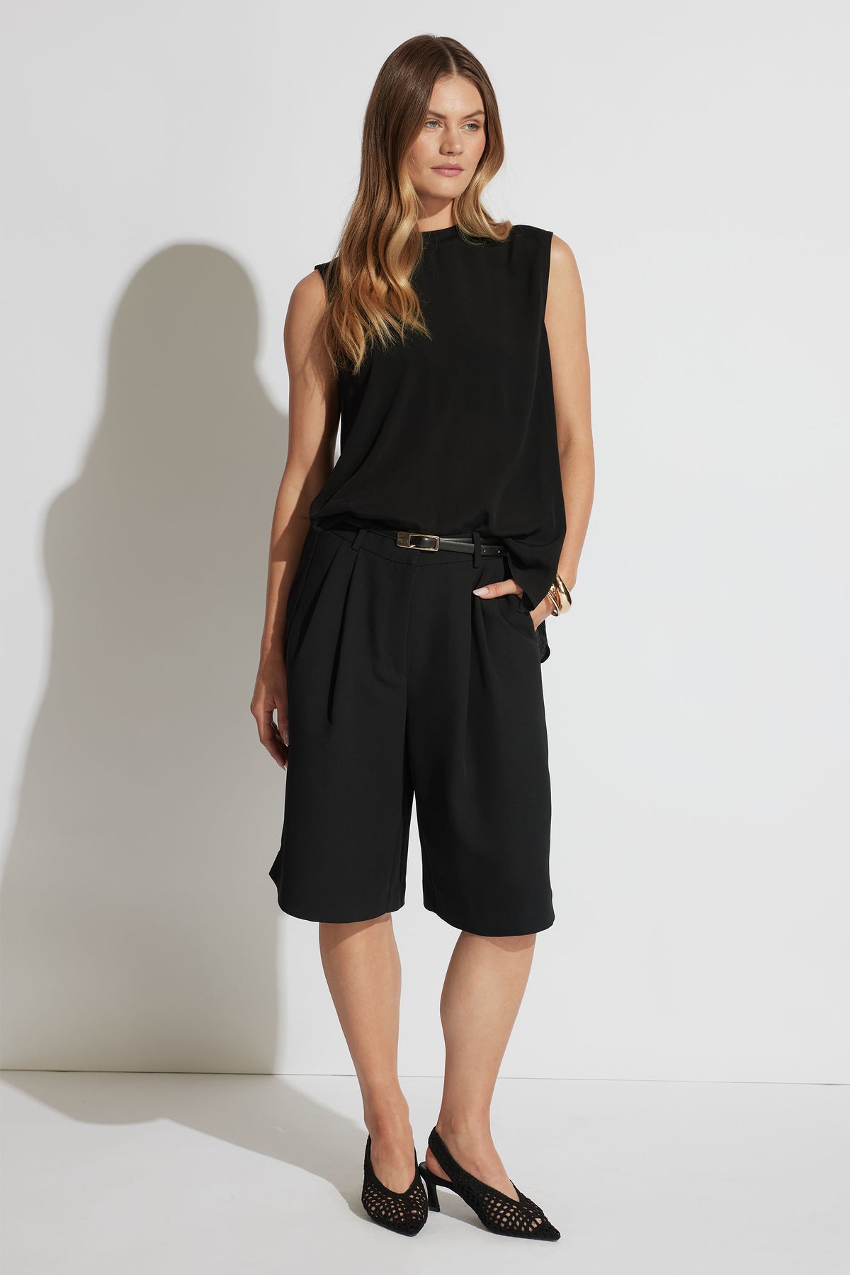 Woman wearing a sleeveless black woven tank paired with high-waisted wide-leg knee-length shorts and black heels