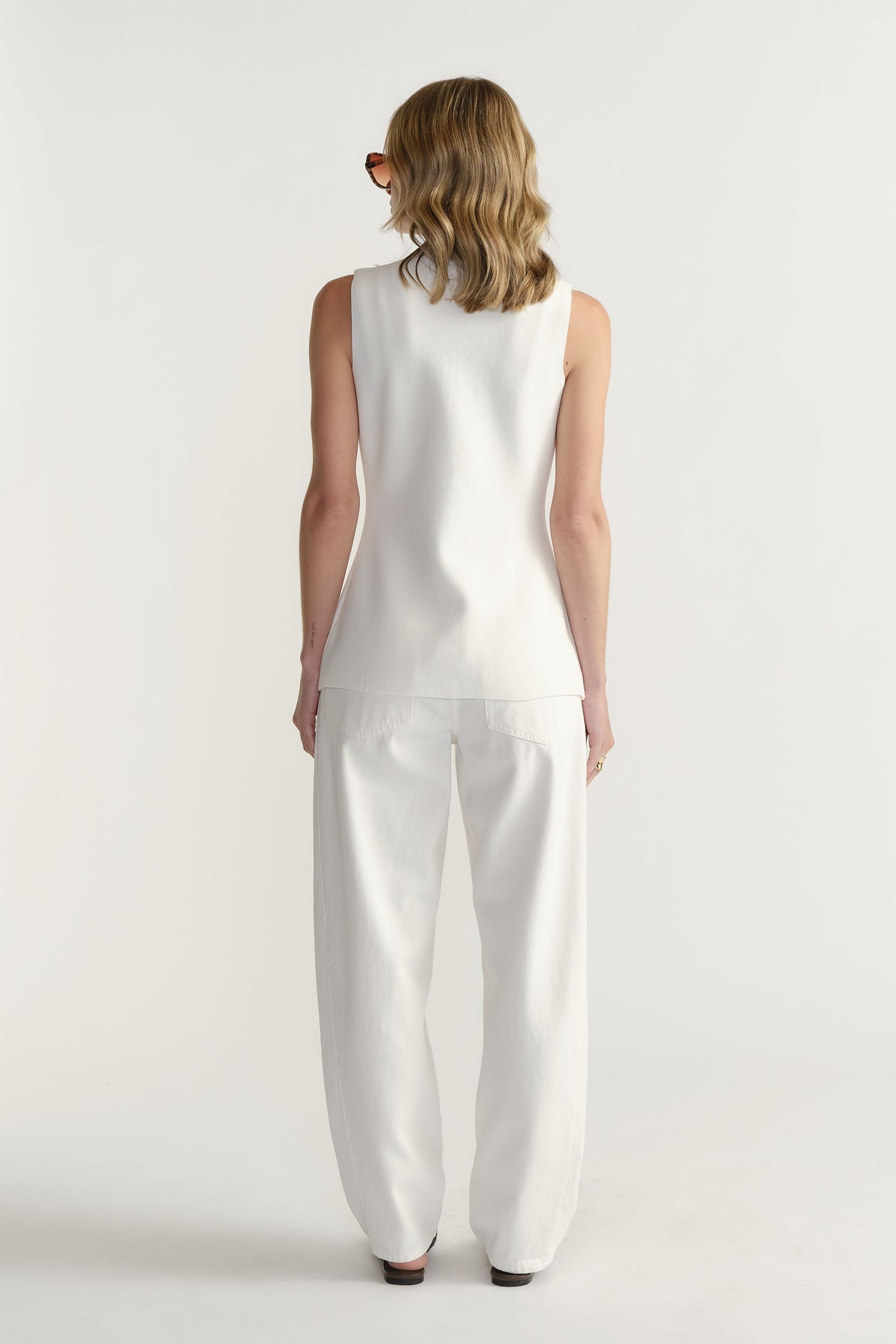 Back view portrait of model wearing Maddie Longline Knit Vest in gallery position 3 with white pants, 1880x2820px