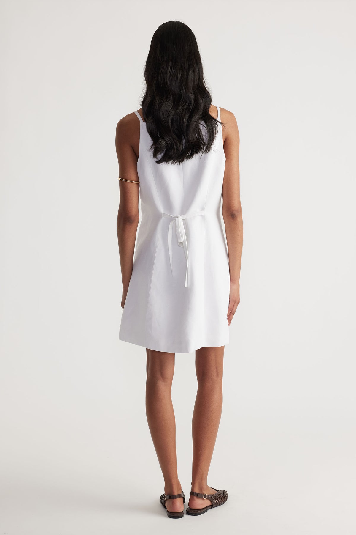 Back view of model wearing white Benne Button Front Vest Dress with tied waist in gallery position 3 portrait orientation