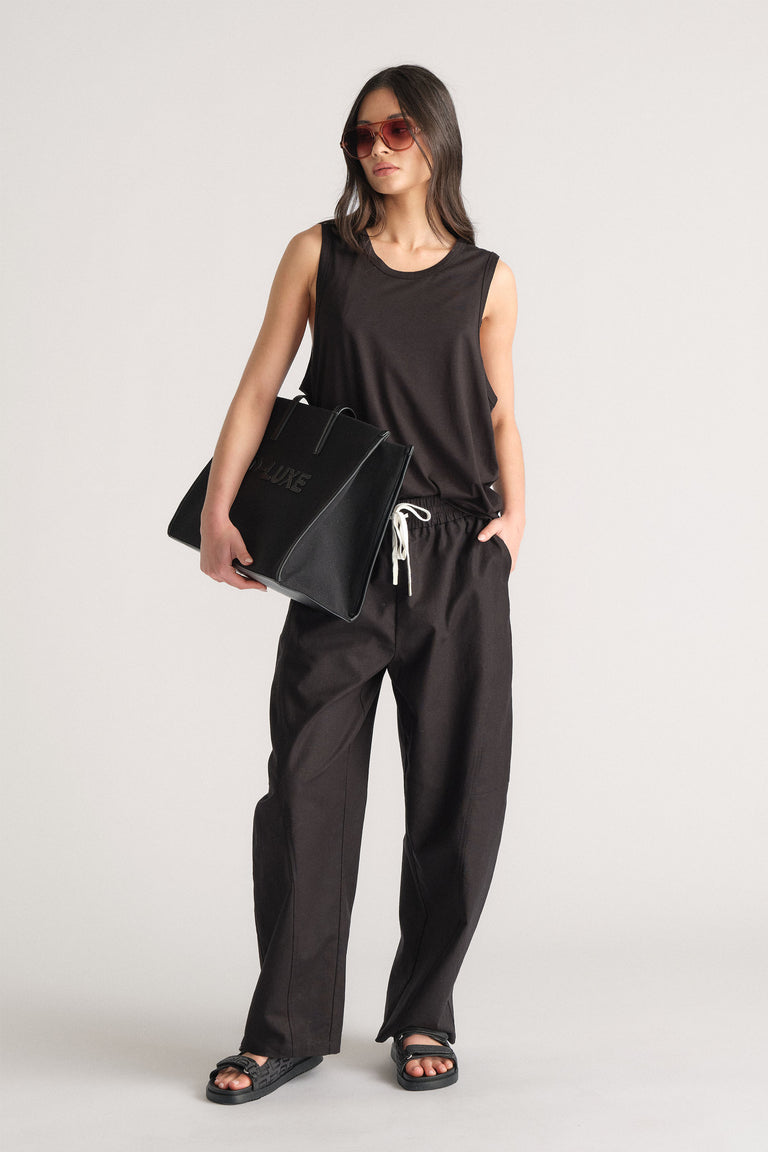Woman wearing a relaxed black sleeveless tank and matching drawstring pants, styled with black sandals and oversized bag.