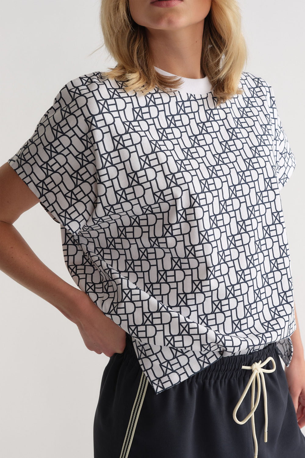 Woman wearing a relaxed fit white tee with an all-over black monogram print paired with casual drawstring pants