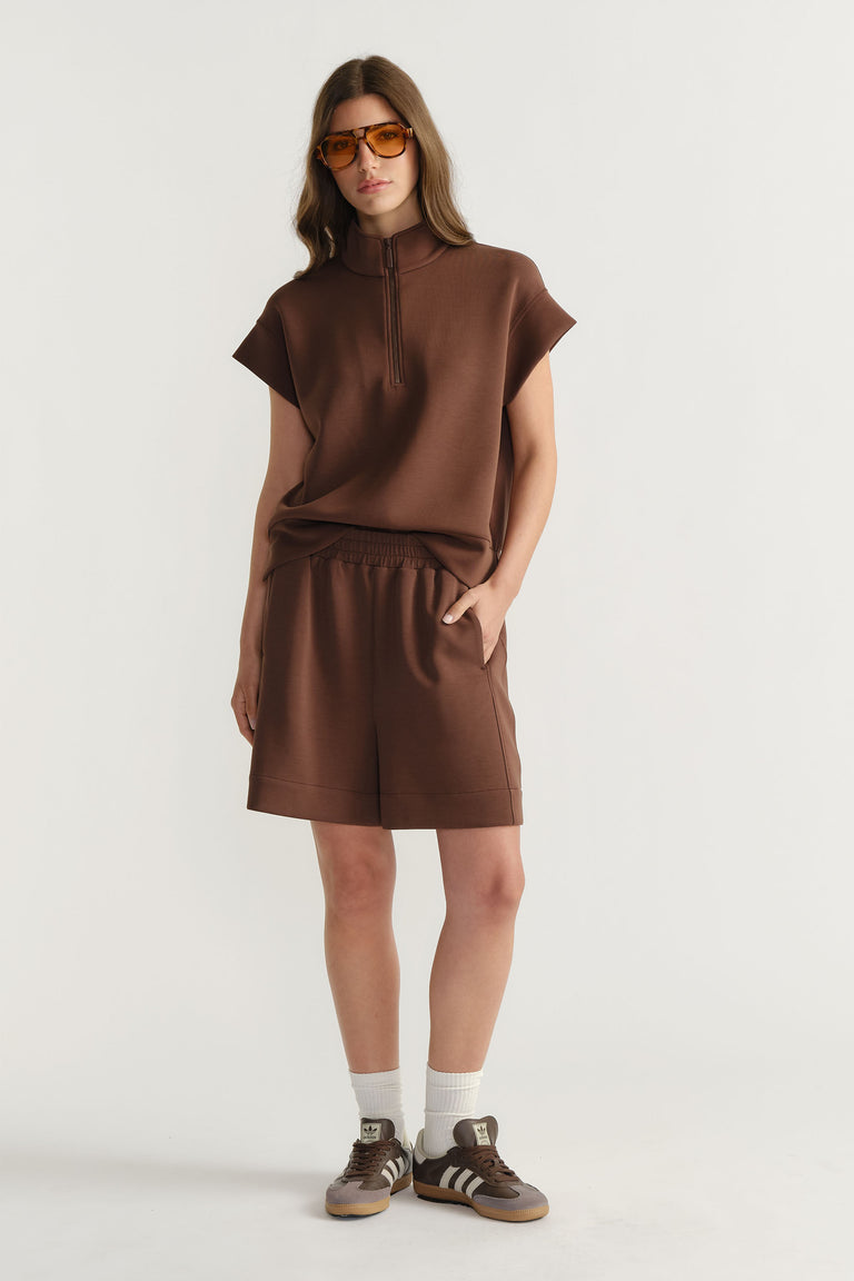 Woman wearing relaxed-fit brown neoprene shorts paired with a matching short-sleeve top and sneakers