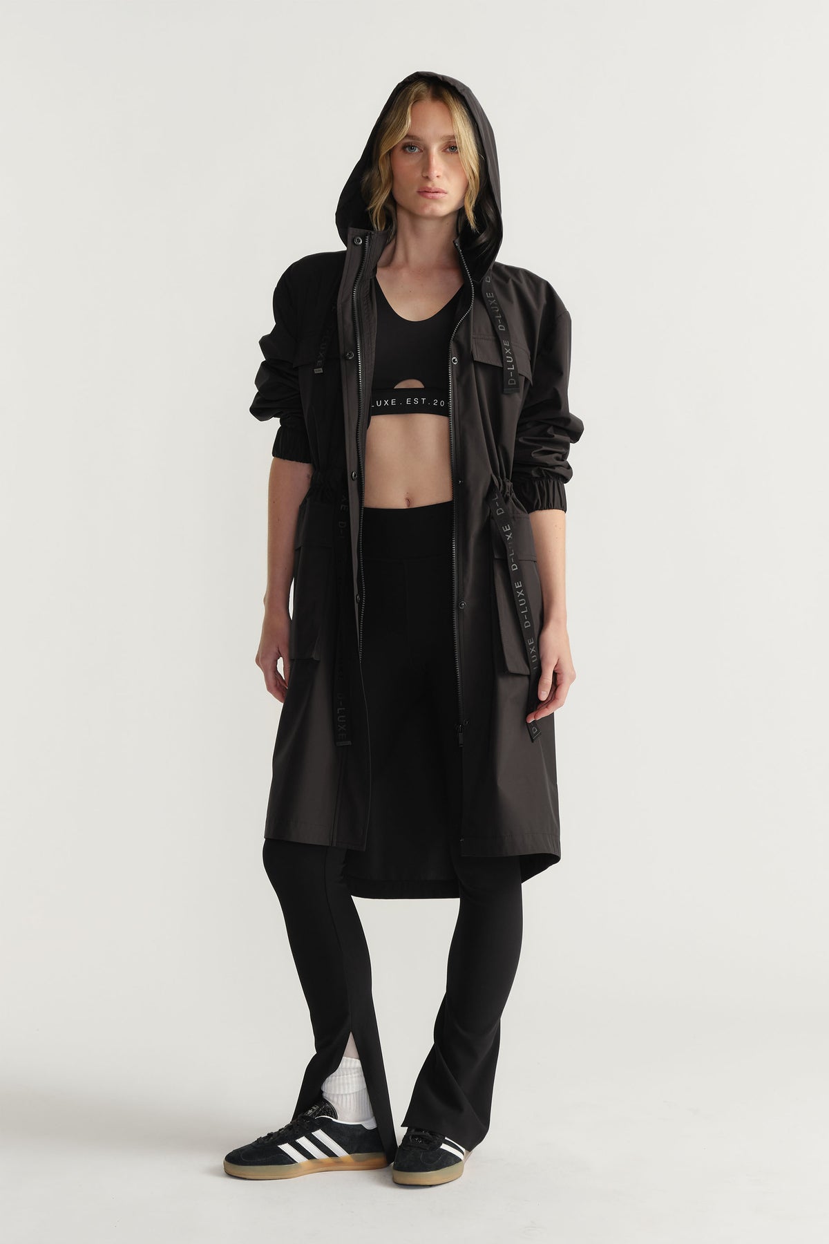Front view of woman wearing black D-Luxe Rain Jacket with hood and drawstring waist styled with black activewear by Decjuba