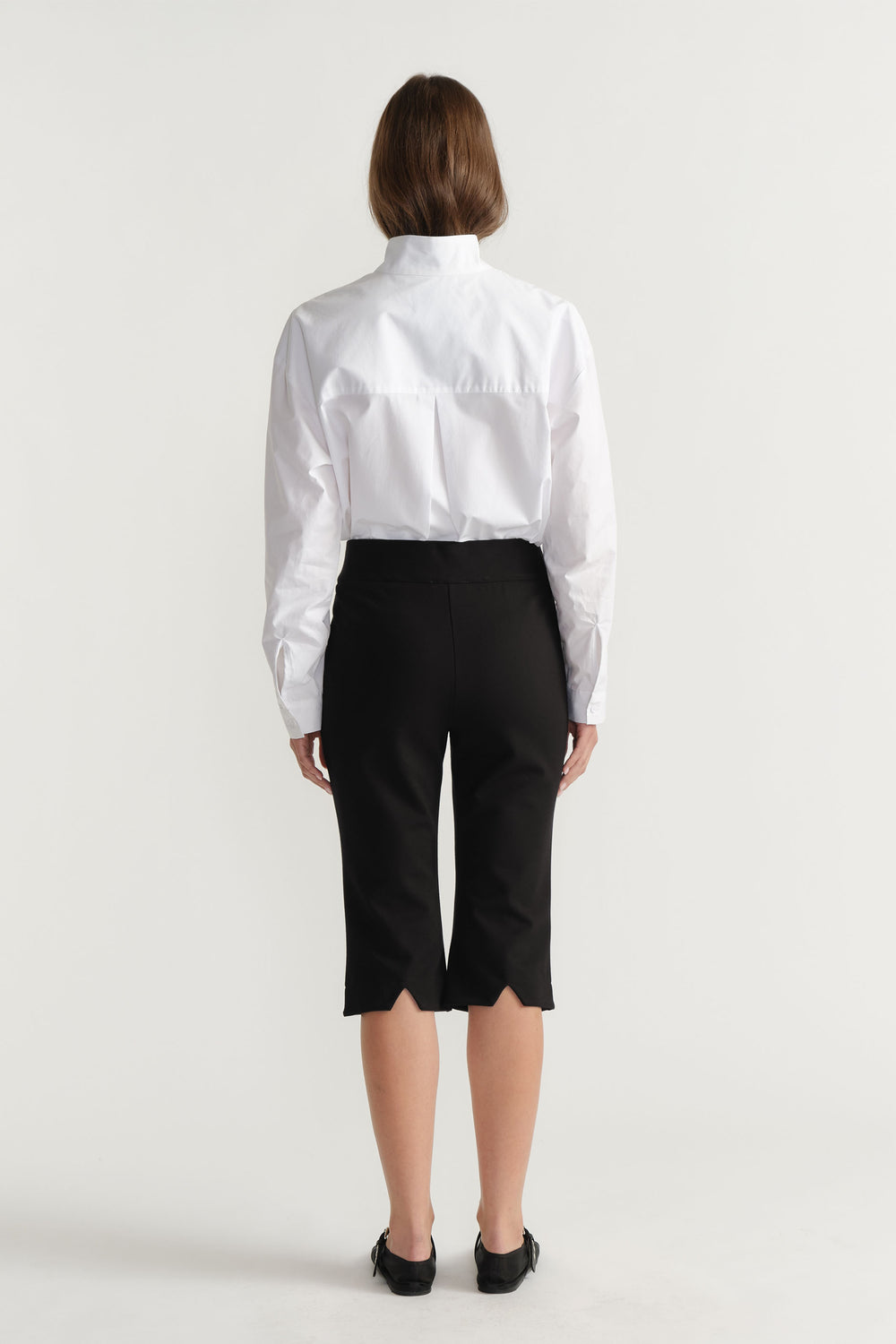 Woman wearing tailored black capri pants with scalloped hems paired with a crisp white long-sleeve shirt