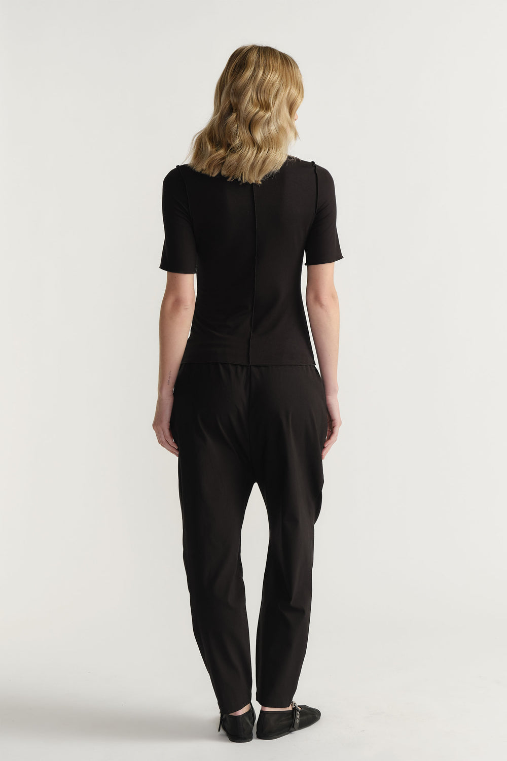 Woman wearing a fitted black short sleeve top paired with relaxed black pants and black pointed shoes from behind view