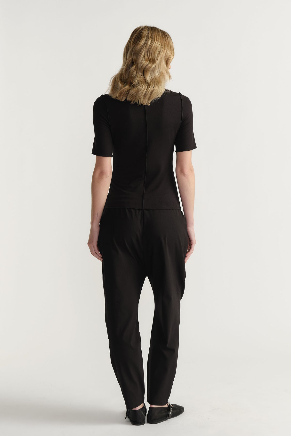 Woman wearing a fitted black short sleeve top paired with relaxed black pants and black pointed shoes from behind view