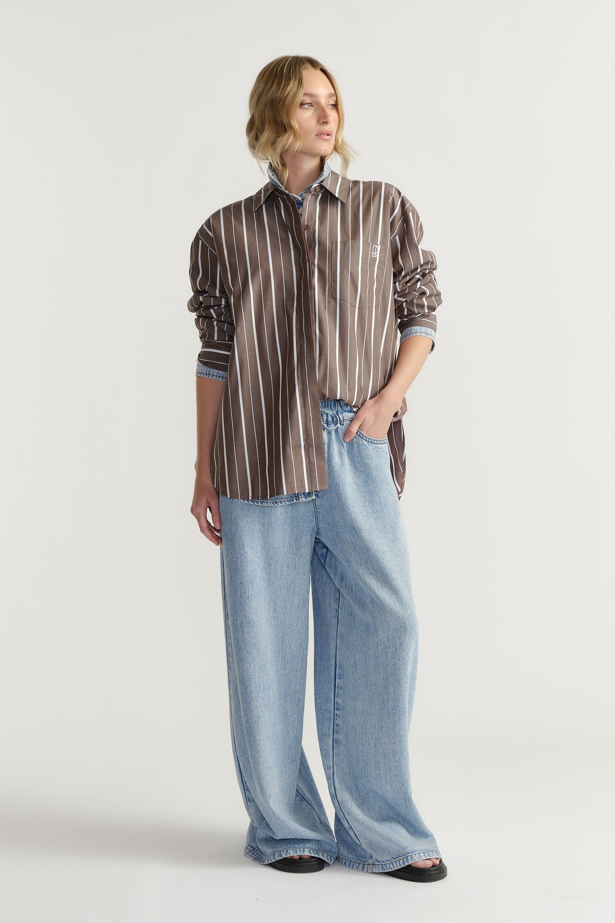 Portrait of model wearing D-Luxe Poplin Stripe Shirt with light blue wide-leg jeans in gallery position 1.