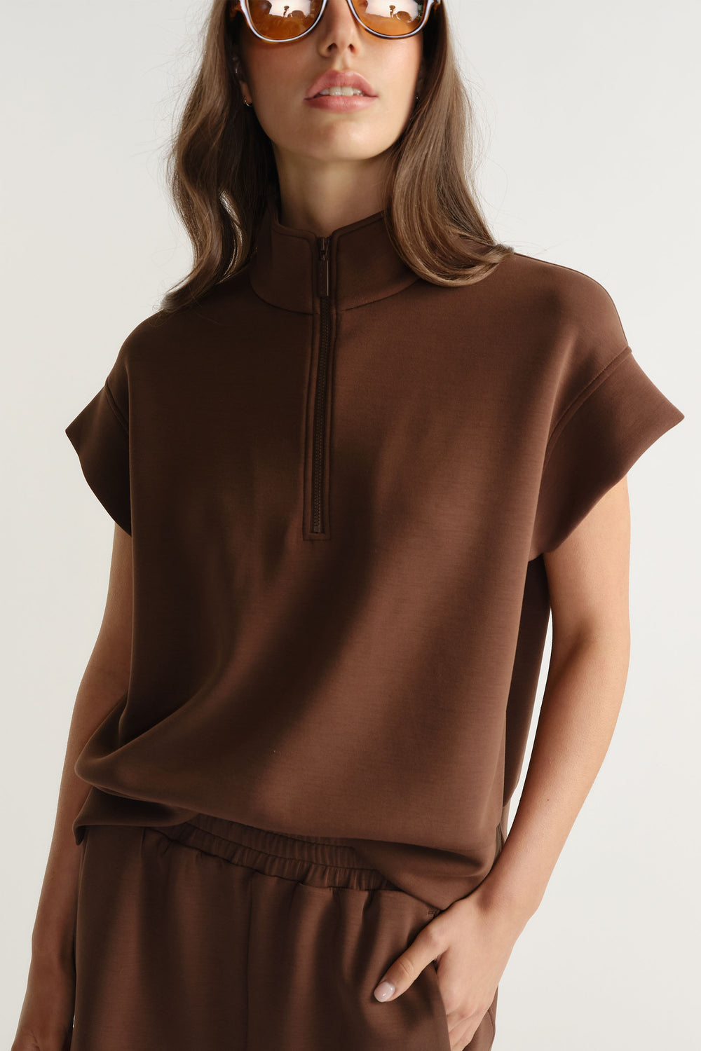 Woman wearing a relaxed fit brown neoprene half zip top with short sleeves and high collar paired with matching bottoms