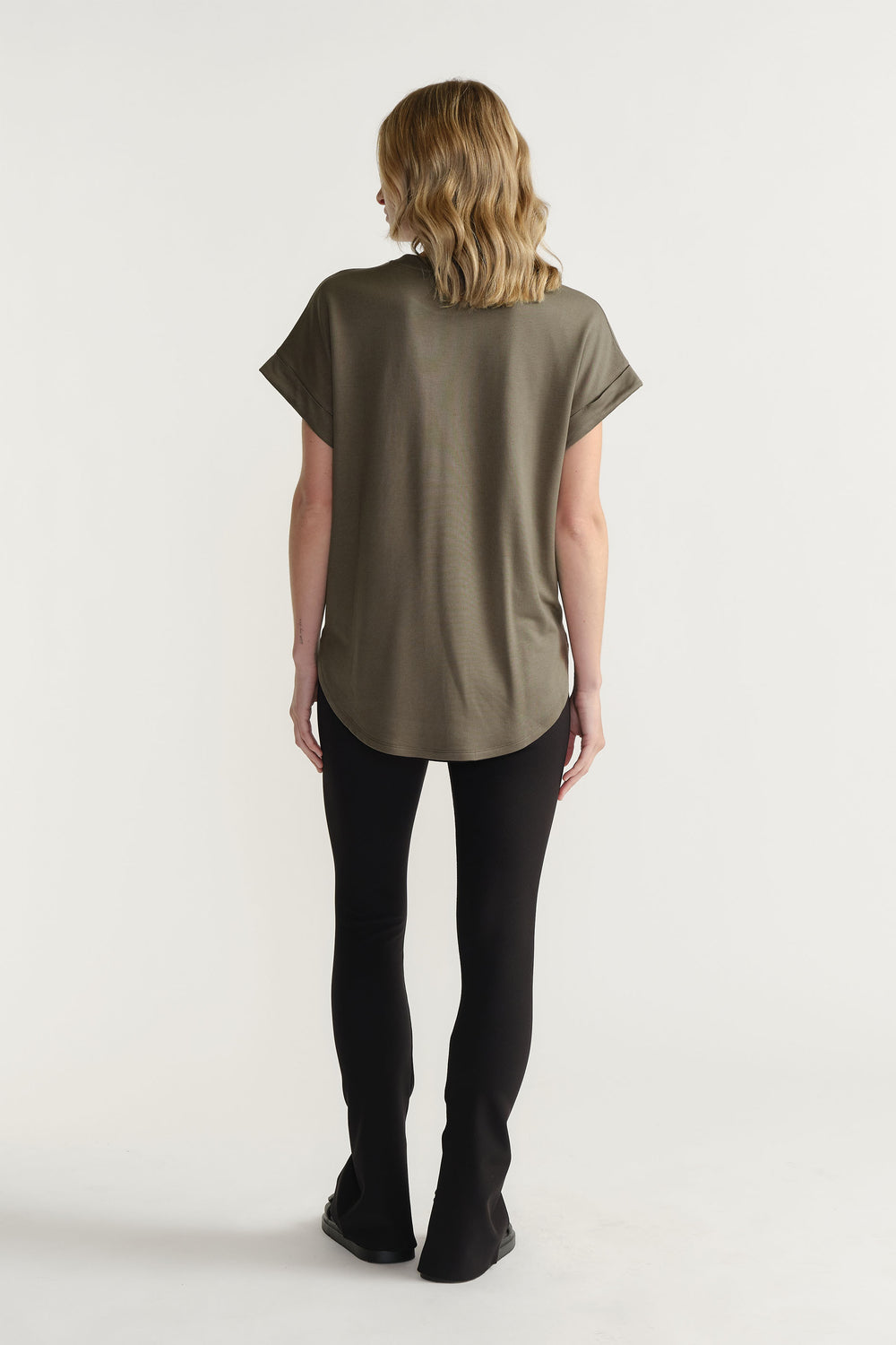 Back view of model wearing D-Luxe Half Moon Tee in olive with turn-back sleeves and high-low hem, gallery position 3.