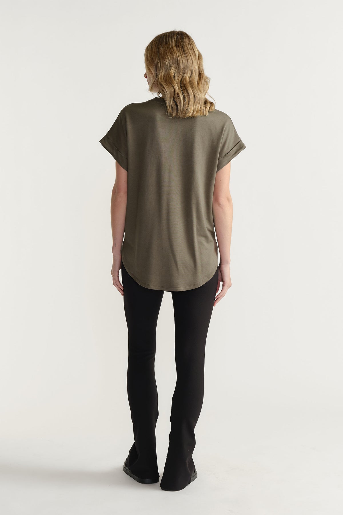 Back view of model wearing D-Luxe Half Moon Tee in olive with turn-back sleeves and high-low hem, gallery position 3.