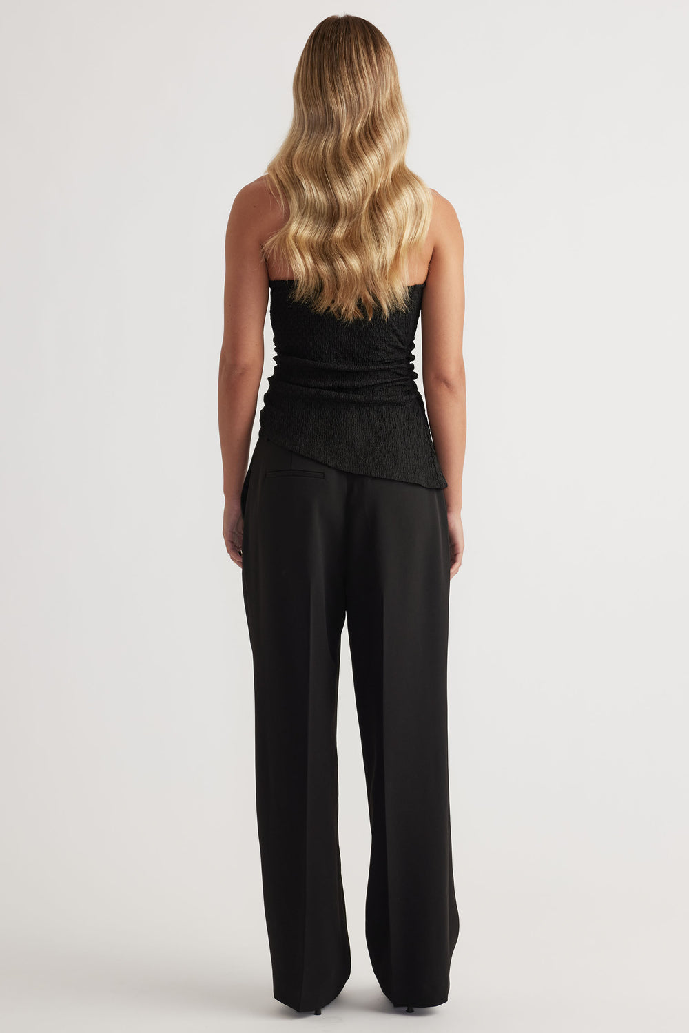 Back view of woman wearing a textured black one-shoulder tank paired with relaxed wide-leg black trousers