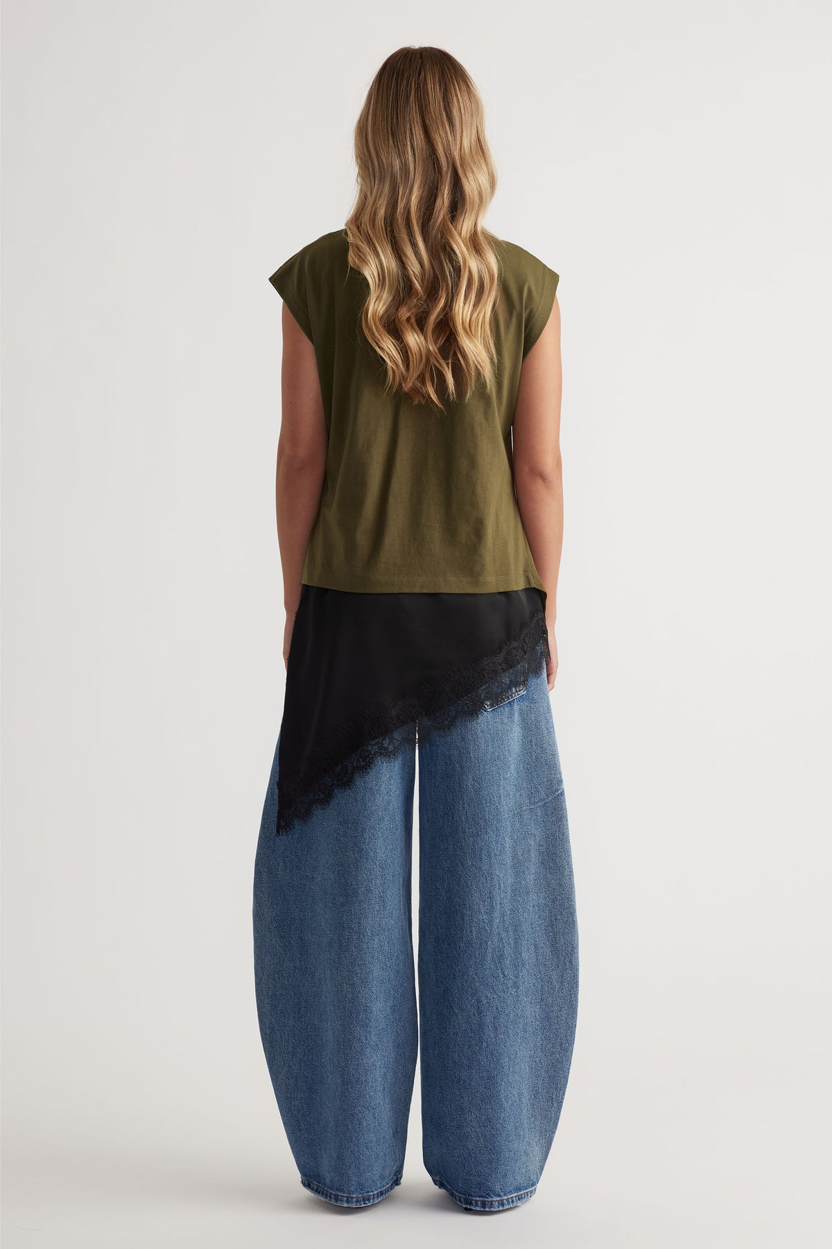Woman shown from behind wearing an olive green twist detail top paired with wide-leg blue denim jeans and a black lace-trim scarf.