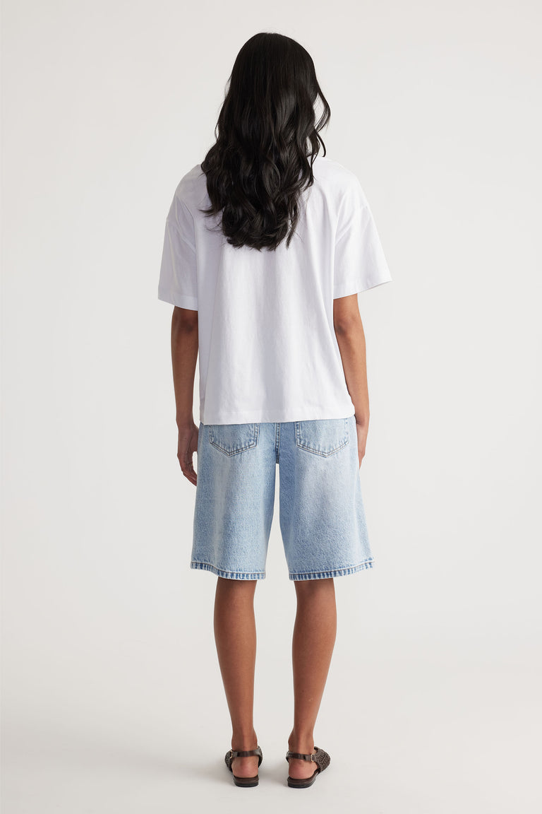 Woman wearing a relaxed white tee paired with light-wash denim shorts and black sandals in a casual outfit.