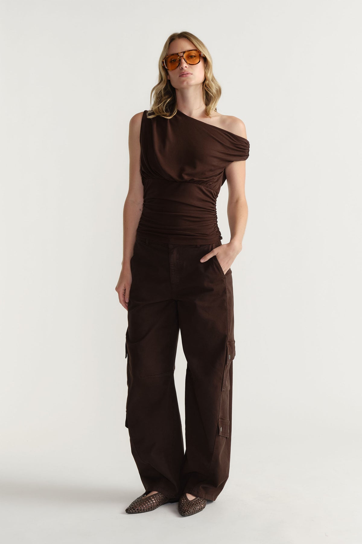 Portrait of model wearing dark brown Alexa Barrel Cargo Pant with side pockets, standing against plain light background.