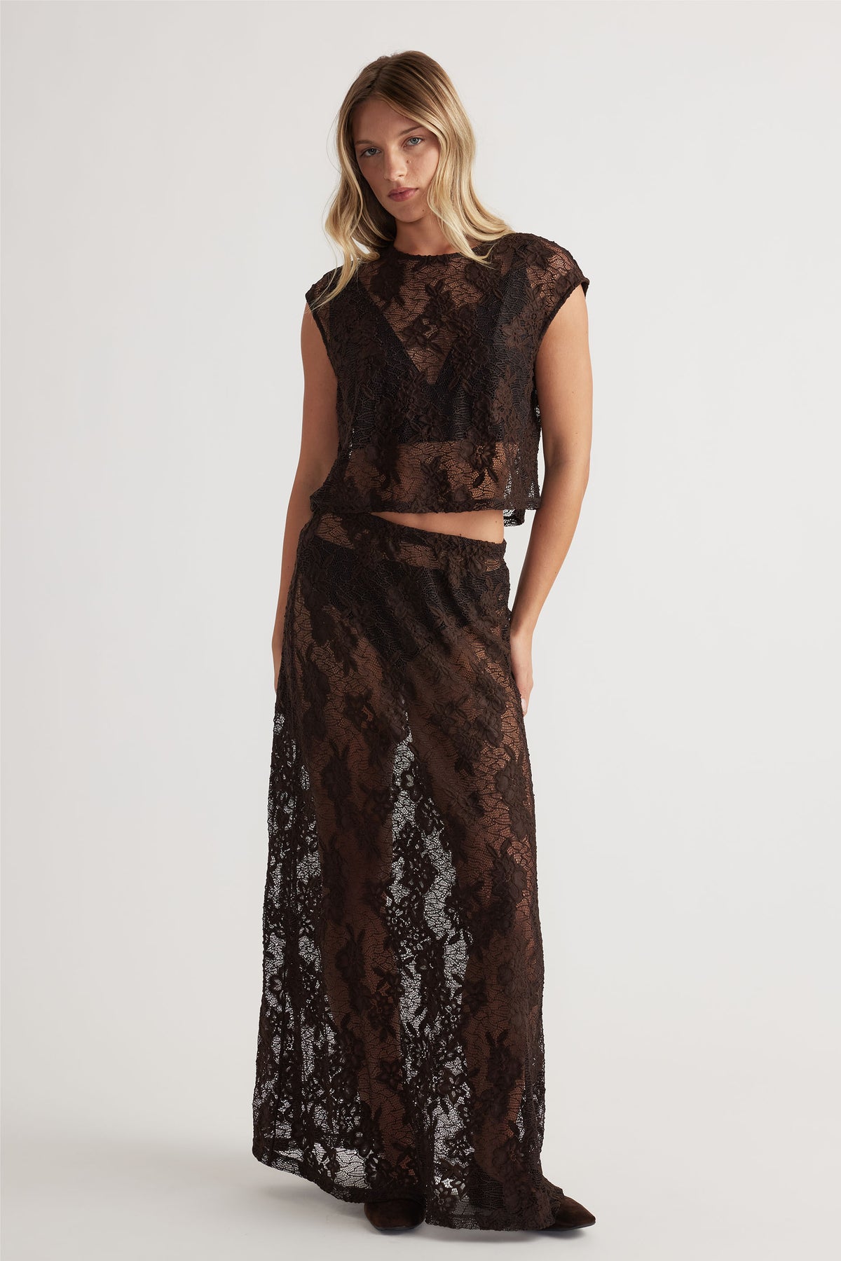 Woman wearing a dark brown sheer lace maxi skirt paired with a matching delicate lace cropped top for an elegant look