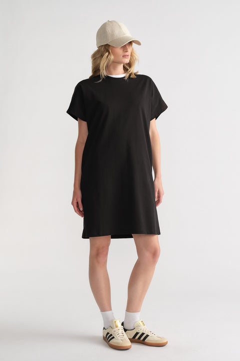 Woman wearing a relaxed black tee dress paired with white socks, retro sneakers, and a beige baseball cap