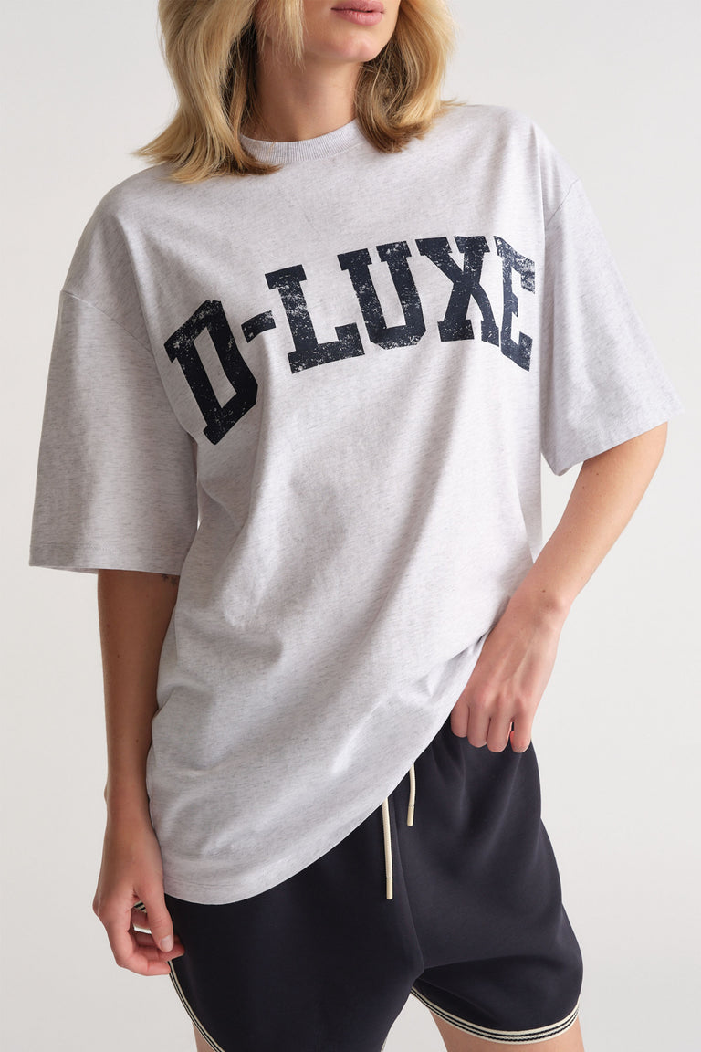 Woman wearing a relaxed fit light grey tee with distressed bold logo paired with casual black drawstring shorts