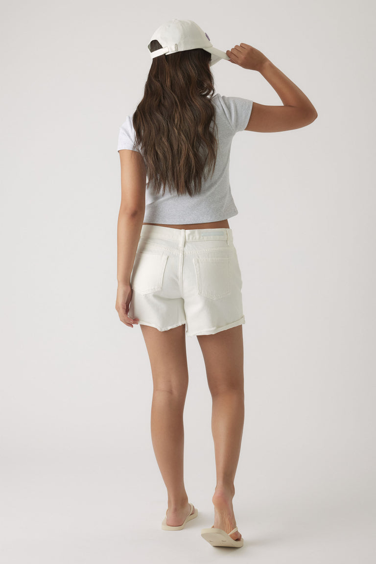 Girl wearing white denim shorts with raw hem paired with a grey crop top and white cap, casual summer look