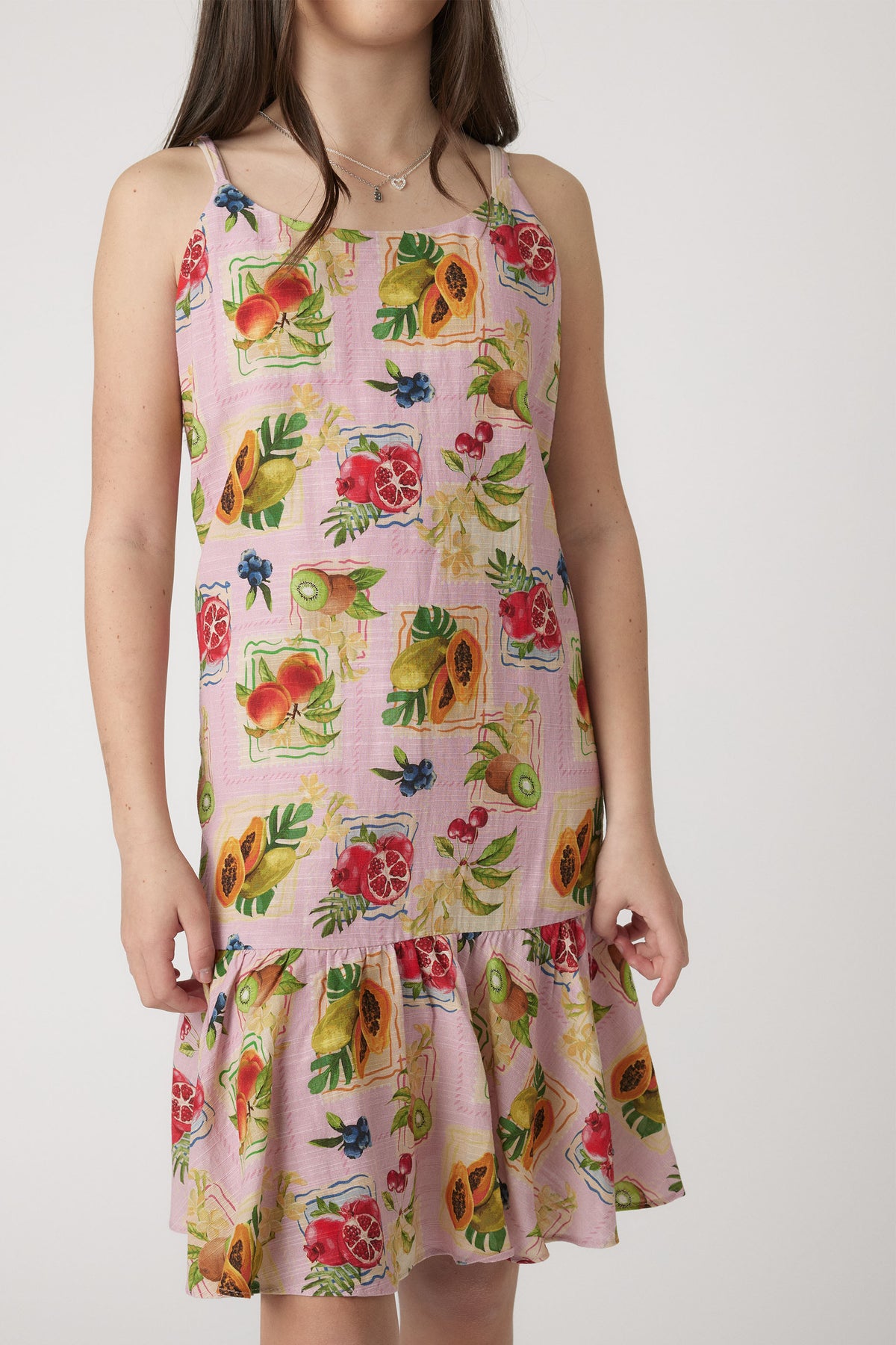 Young girl wearing a sleeveless dress with a colorful tropical fruit print and ruffled hem for playful style