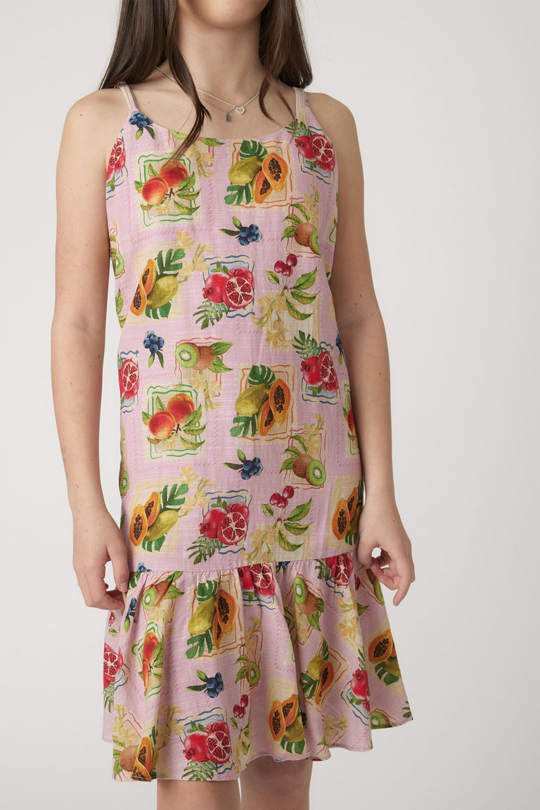 Young girl wearing a sleeveless dress with a colorful tropical fruit print and ruffled hem for playful style