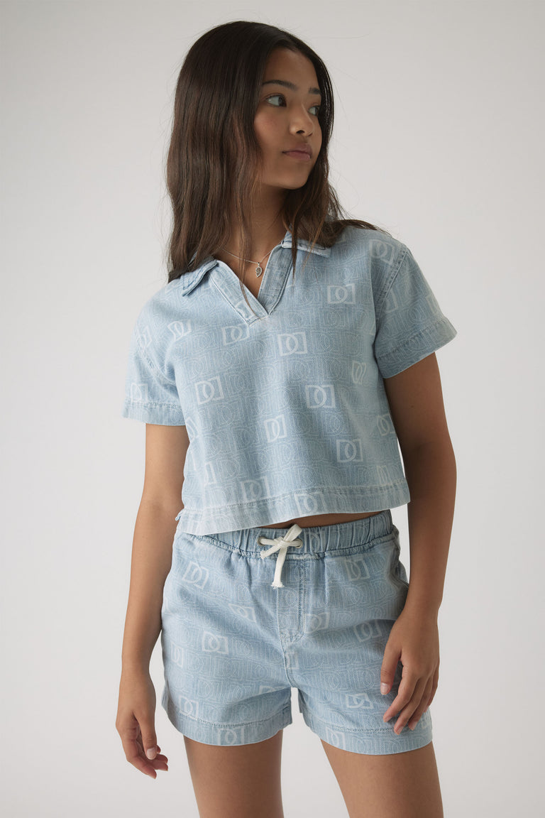 Girl wearing light blue denim short set with subtle monogram print and relaxed collared short sleeve top.
