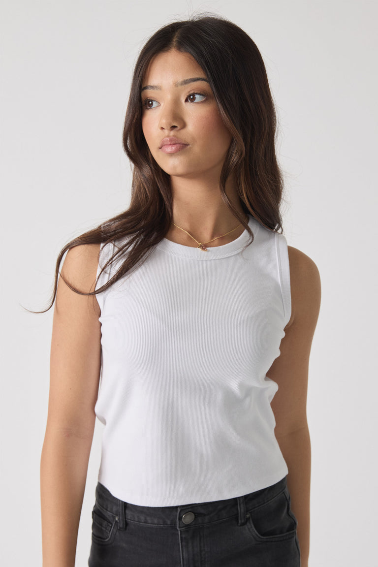Teen girl wearing a white Girls Harper Logo Tank paired with black jeans, showcasing a versatile style by Decjuba Australian brand