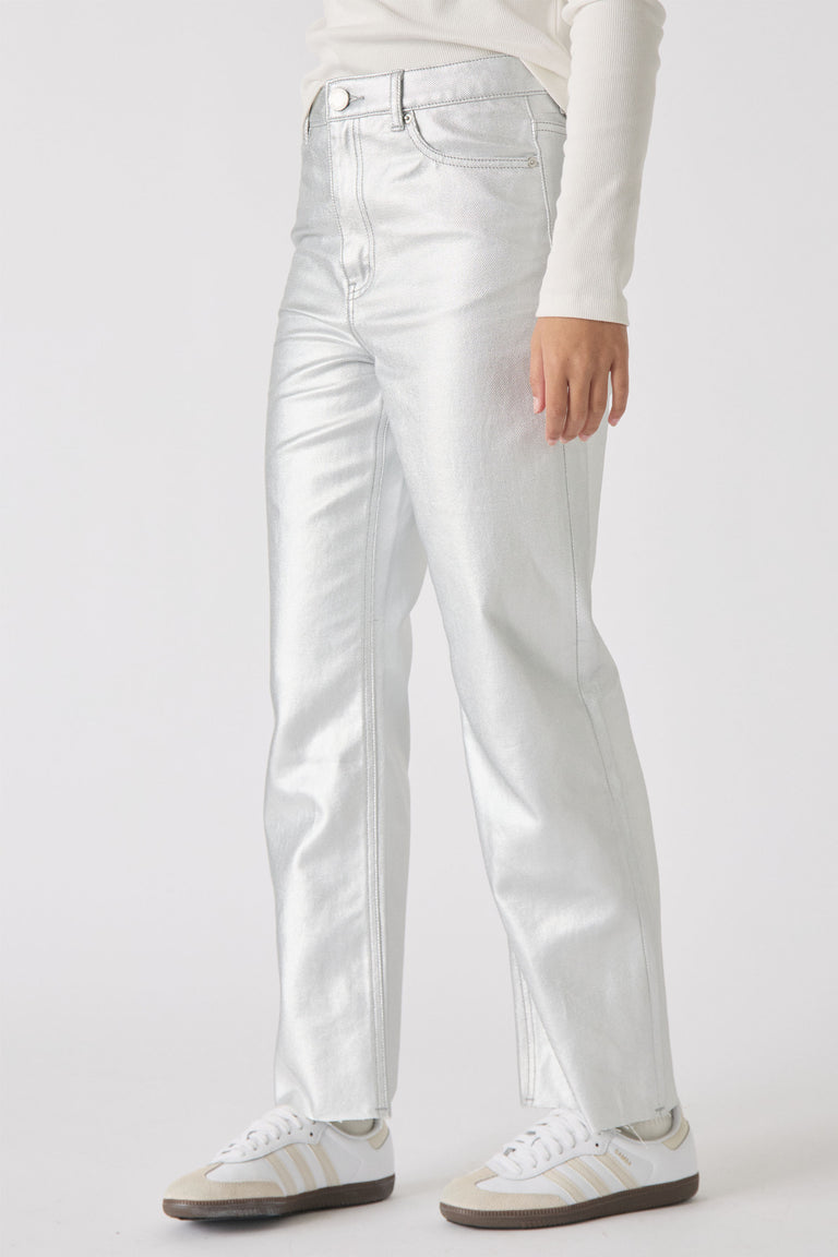Girl wearing silver straight leg jeans paired with white top and white sneakers, standing against plain background