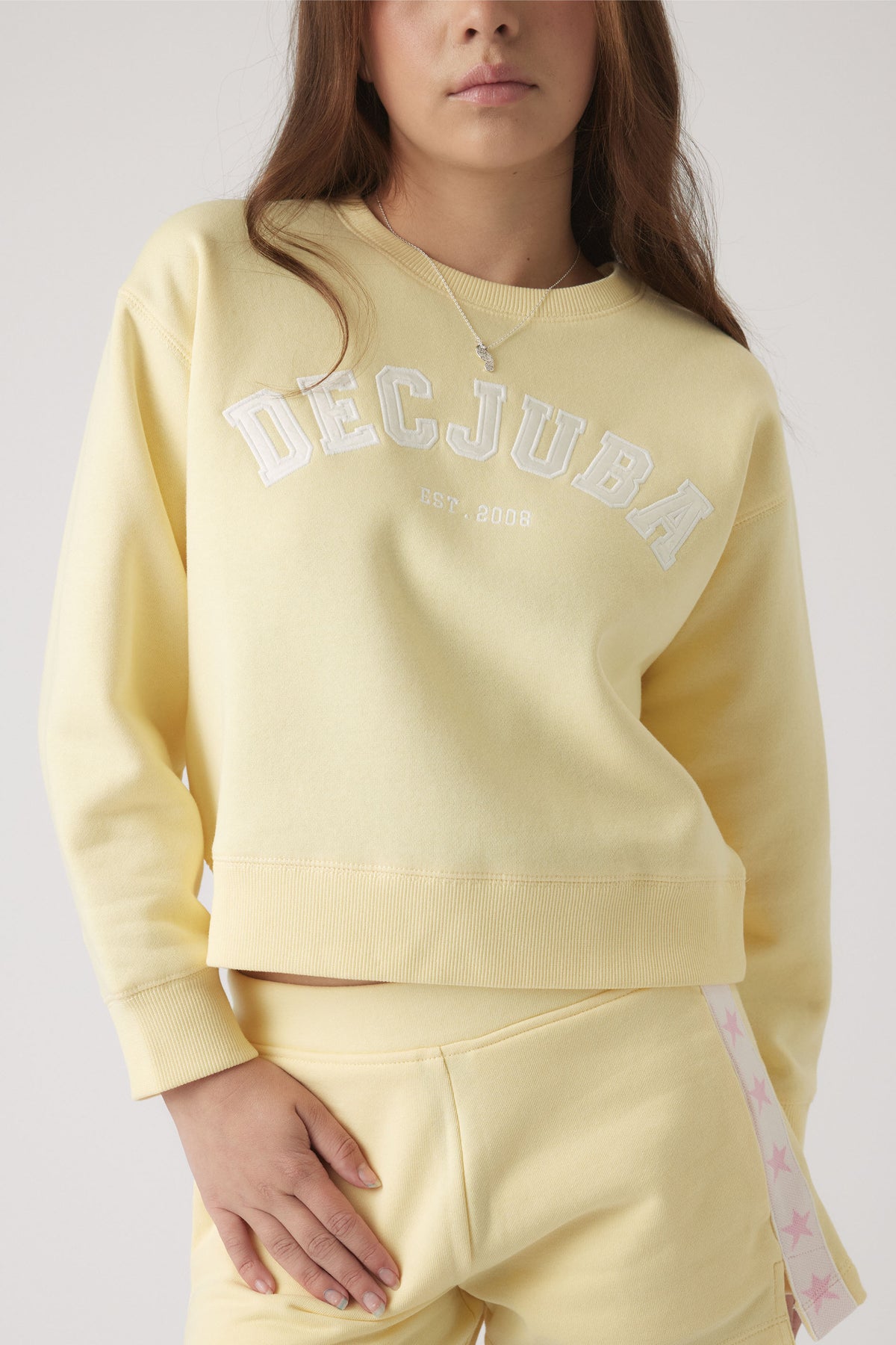 Girl wearing a soft yellow logo sweatshirt with matching pants featuring a star-patterned side stripe detail.