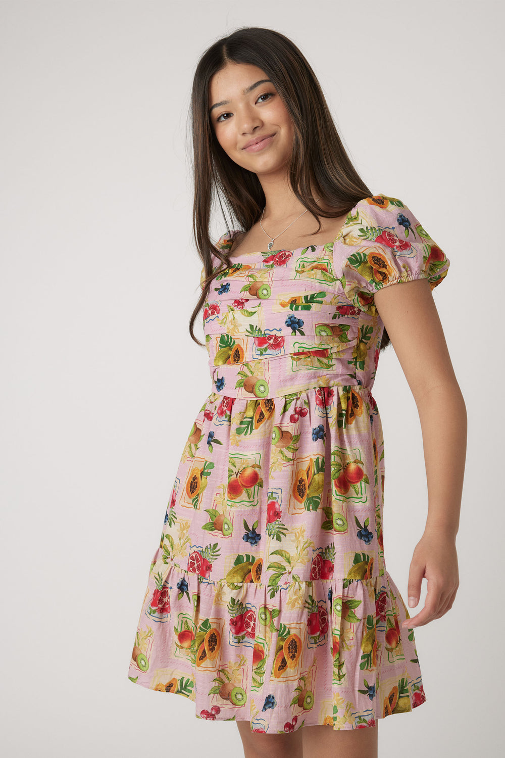 Girl wearing a pink mini dress with puff sleeves featuring a colorful fruit and floral print for casual wear