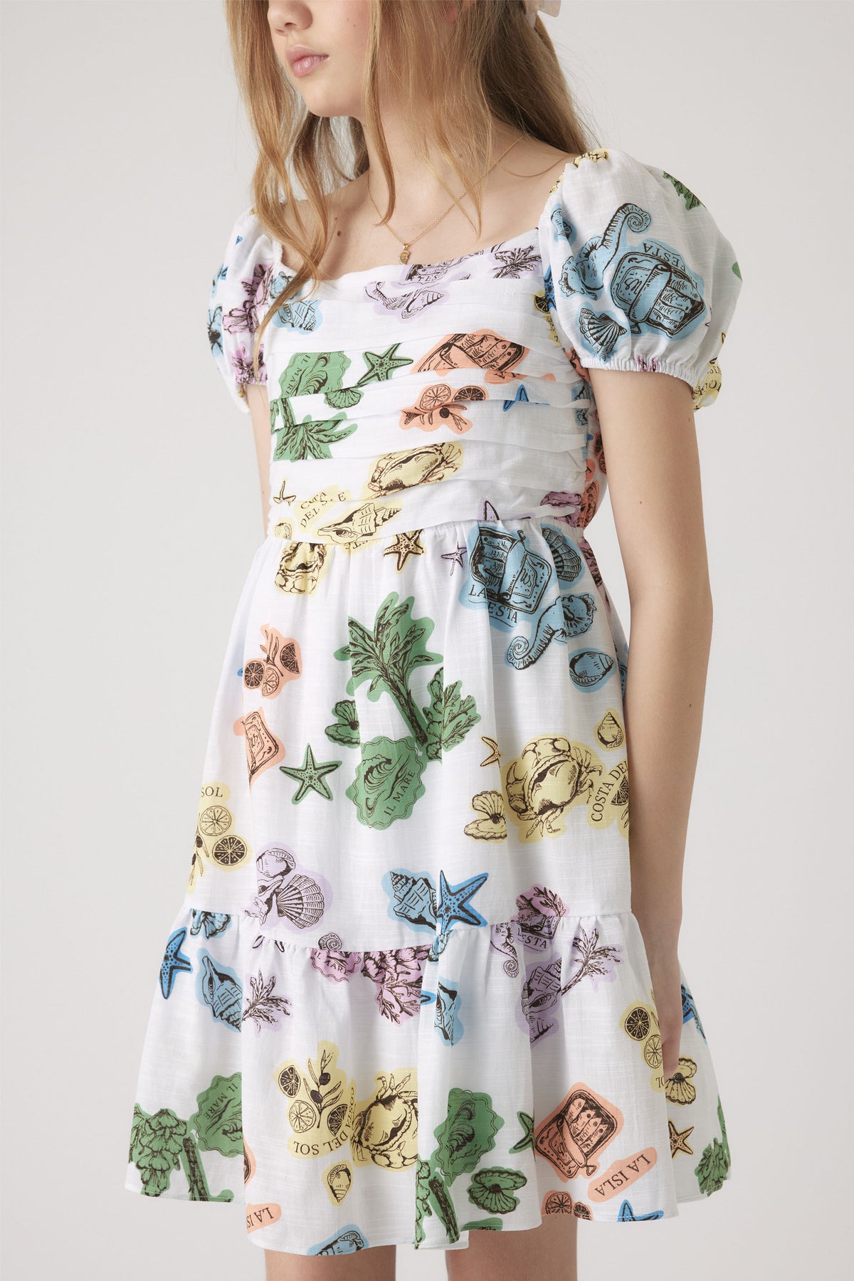 Girl wearing a white mini dress with colorful sea life illustrations and puff sleeves, featuring a square neckline and gathered bodice.
