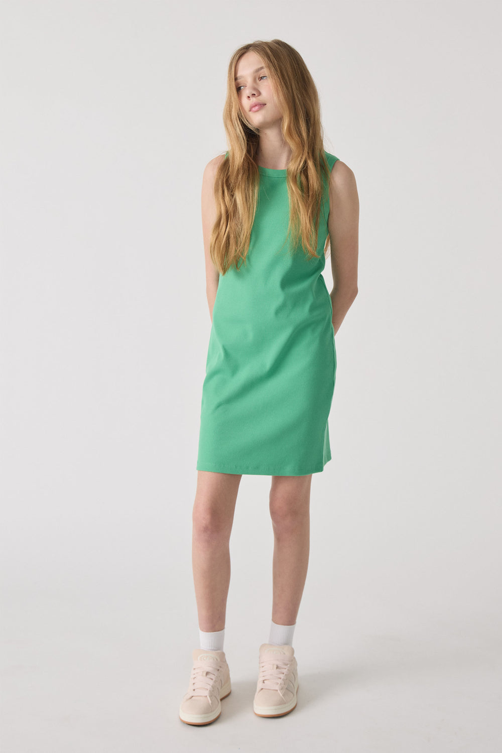 Girl wearing a sleeveless spring green ribbed tank dress paired with white socks and cream sneakers in a minimalist setting