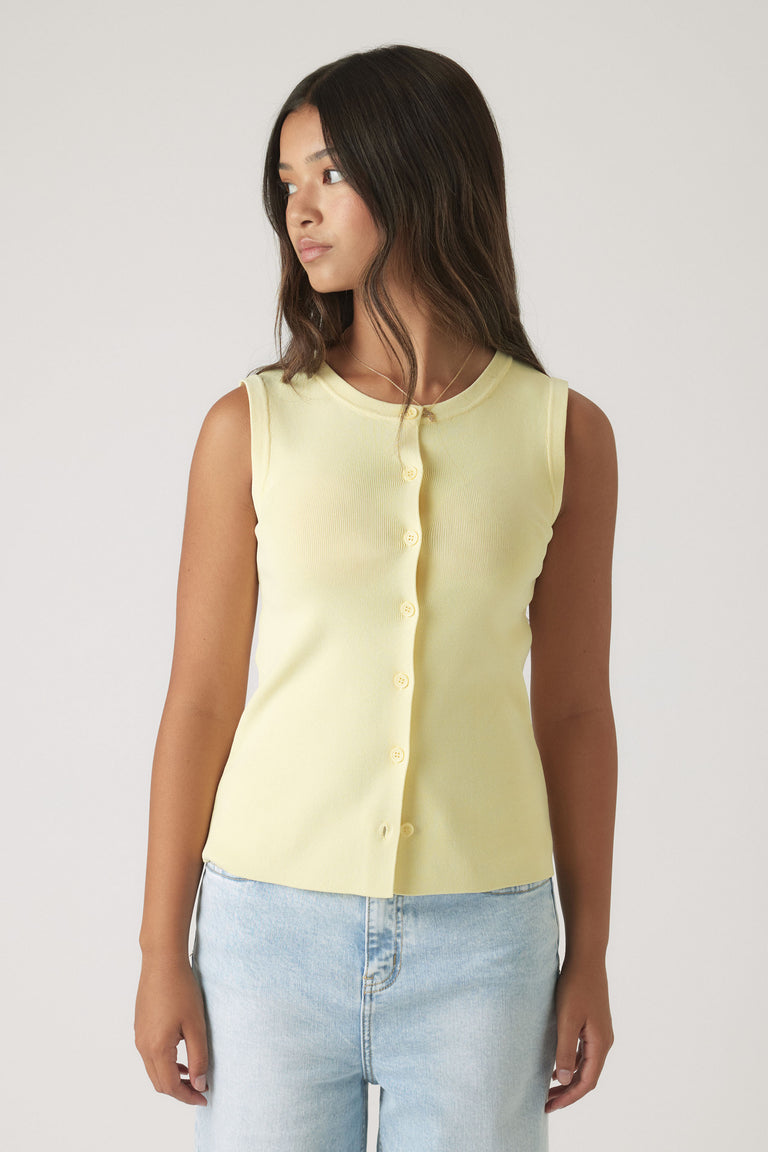 Girl wearing a soft yellow sleeveless button-up knit vest paired with light wash denim jeans against a neutral background