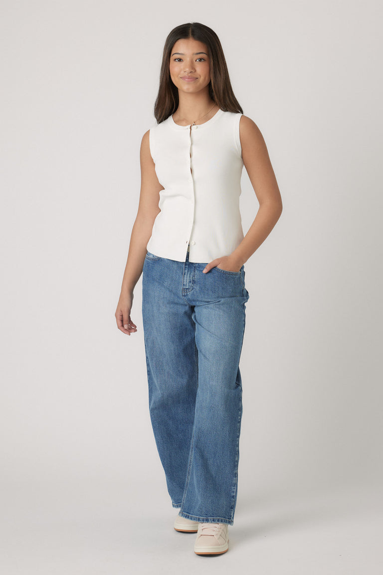 Girl wearing a sleeveless cream knit vest with button front, paired with relaxed wide-leg blue jeans and casual sneakers