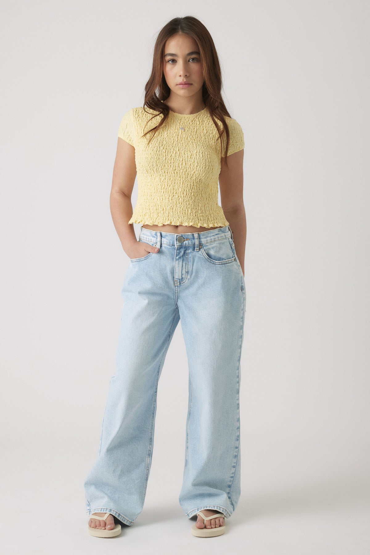 Teen girl wearing a textured lemon yellow cropped top paired with loose light wash wide-leg jeans and sandals