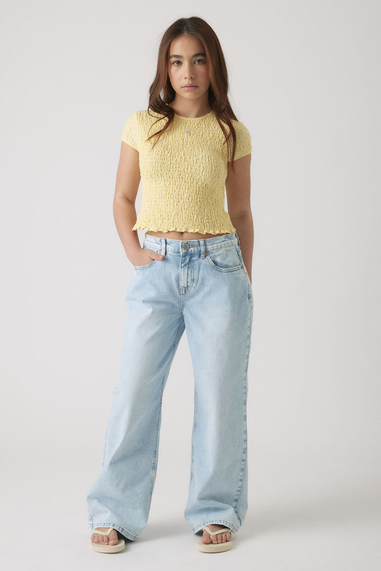 Teen girl wearing a textured lemon yellow cropped top paired with loose light wash wide-leg jeans and sandals