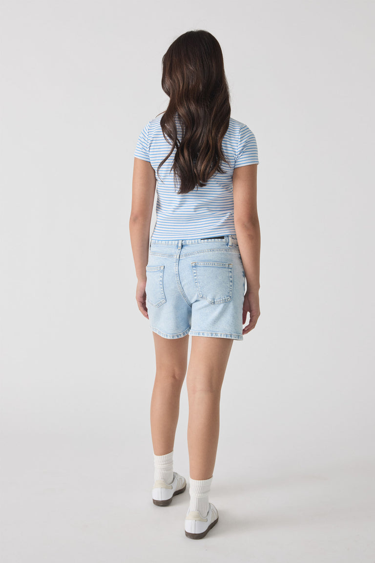 Girl wearing light blue denim shorts paired with a striped short-sleeve top and white sneakers, shown from behind.