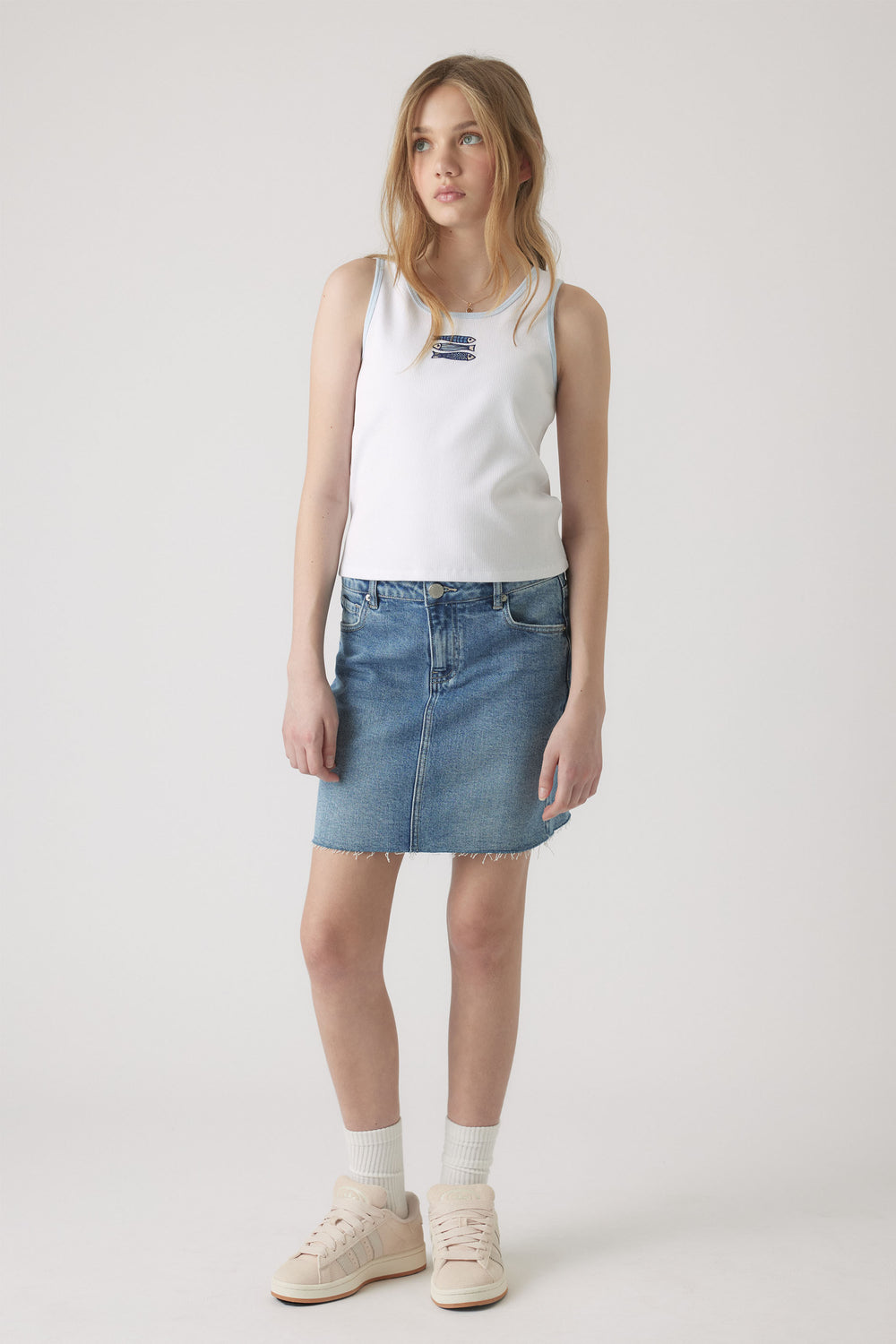 Girl wearing a white embroidered tank top paired with a casual blue denim skirt and light sneakers