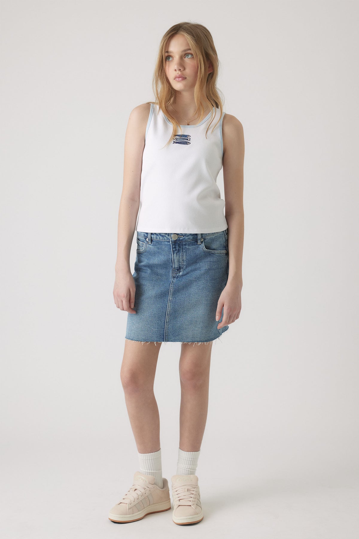 Girl wearing a white embroidered tank top paired with a casual blue denim skirt and light sneakers