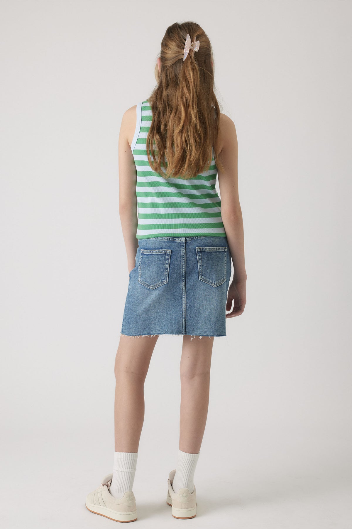 Girl wearing a green and white striped tank paired with a light blue denim skirt, white socks, and sneakers.