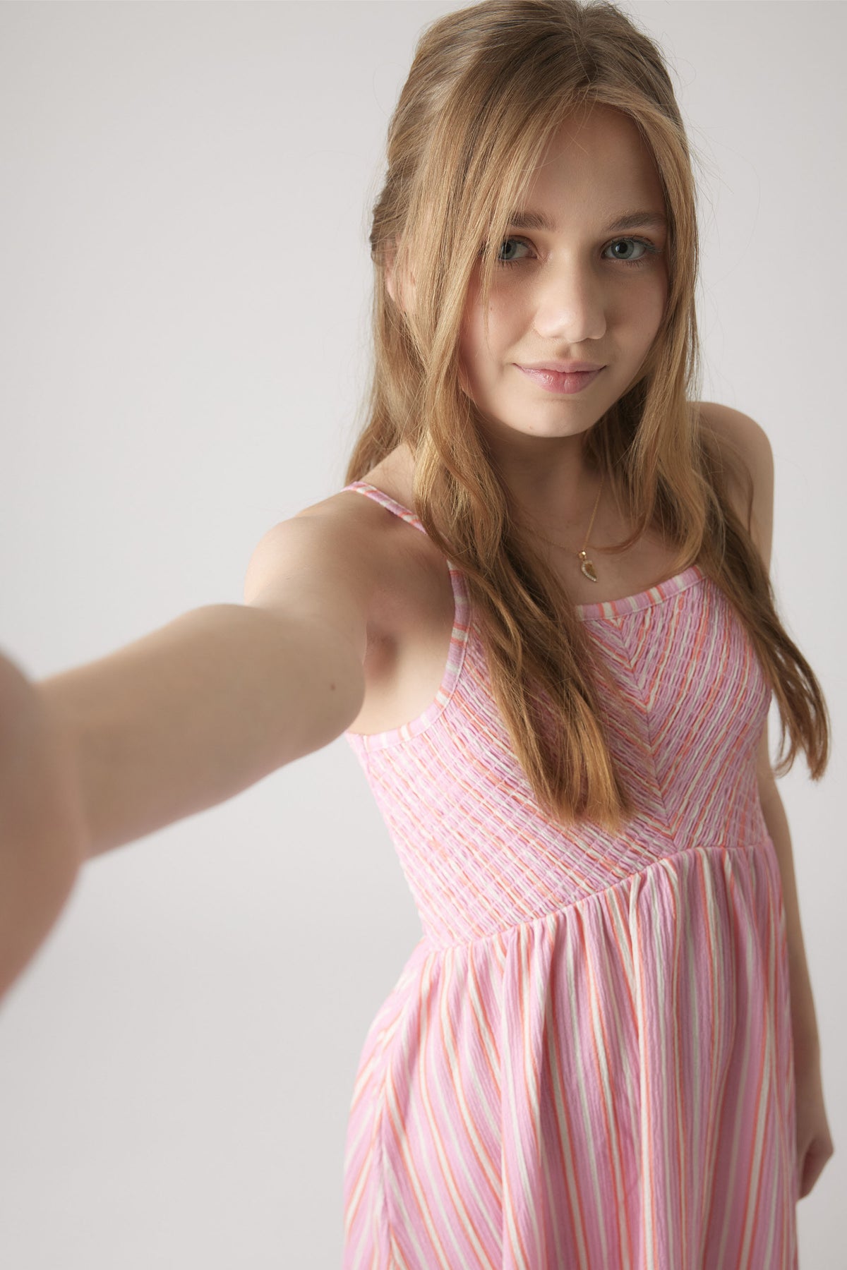 Girl taking a selfie wearing a pink striped shirred dress with thin straps and a relaxed skirt silhouette