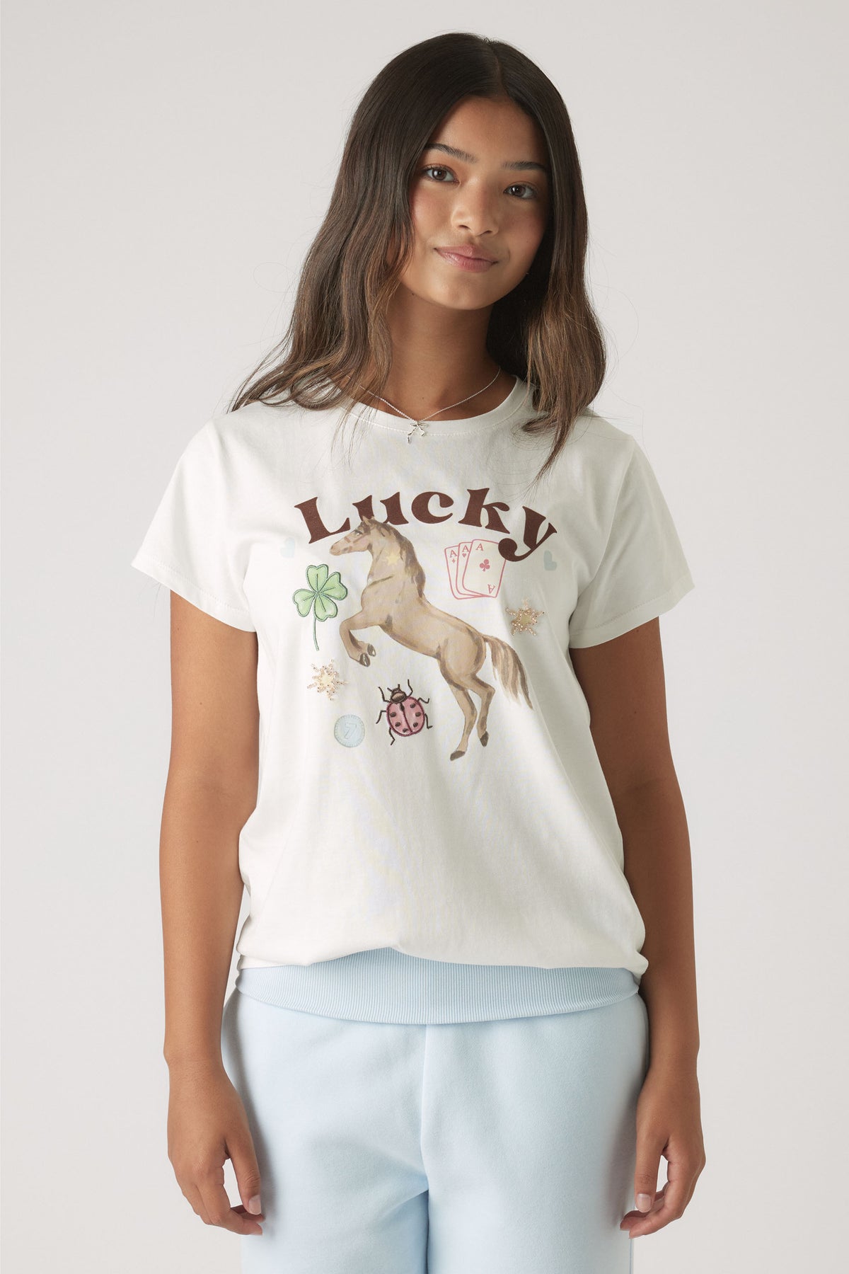 Girl wearing a white tee featuring a horse and lucky symbols paired with relaxed light blue pants for casual style