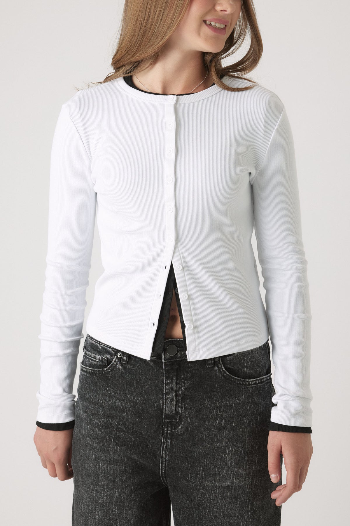 Girl wearing a button-through white Girls Riley Rib Long Sleeve top, fitted rib cotton with black trim, portrait view.