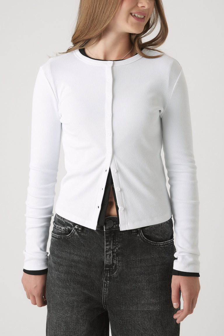 Girl wearing a button-through white Girls Riley Rib Long Sleeve top, fitted rib cotton with black trim, portrait view.