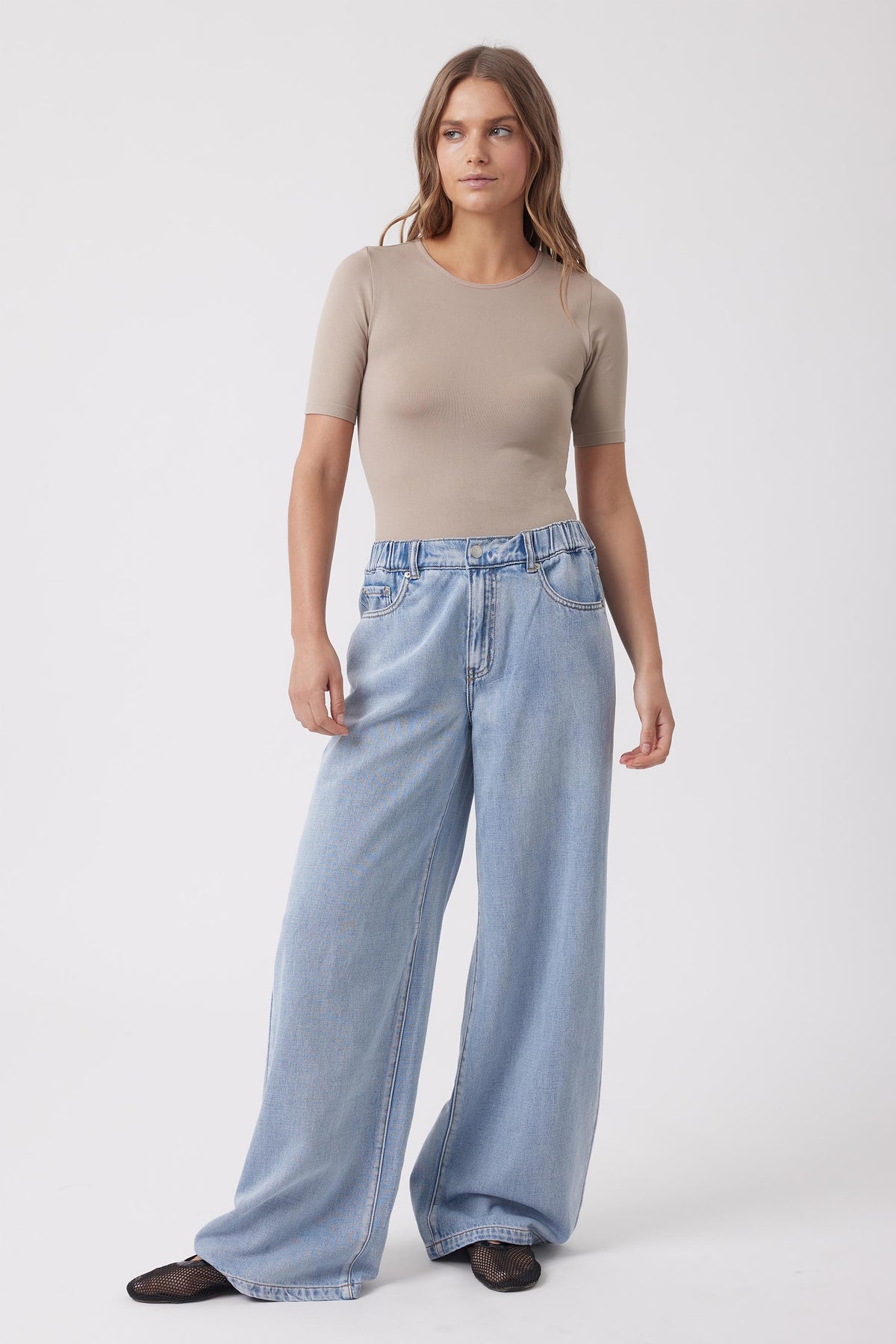 Woman wearing a beige fitted short sleeve tee with light wash wide leg jeans