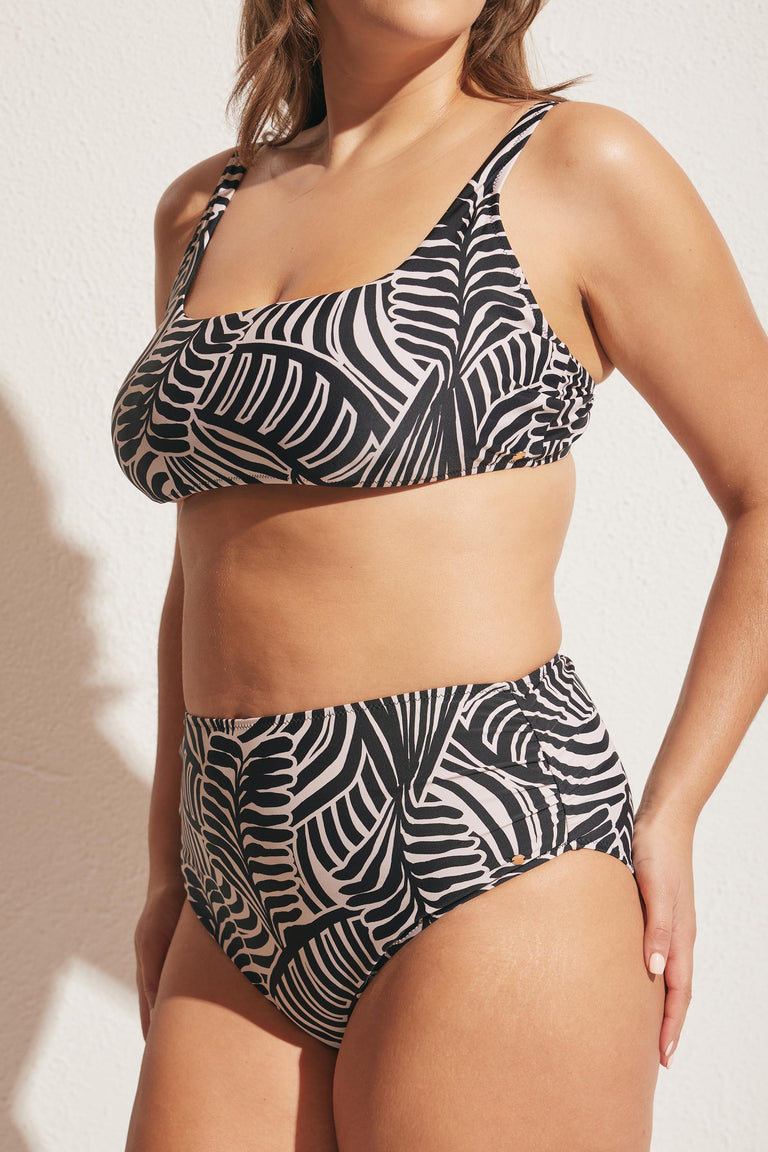 Woman wearing a high-waisted bikini bottom and a matte square neck top with bold black and white tropical leaf print