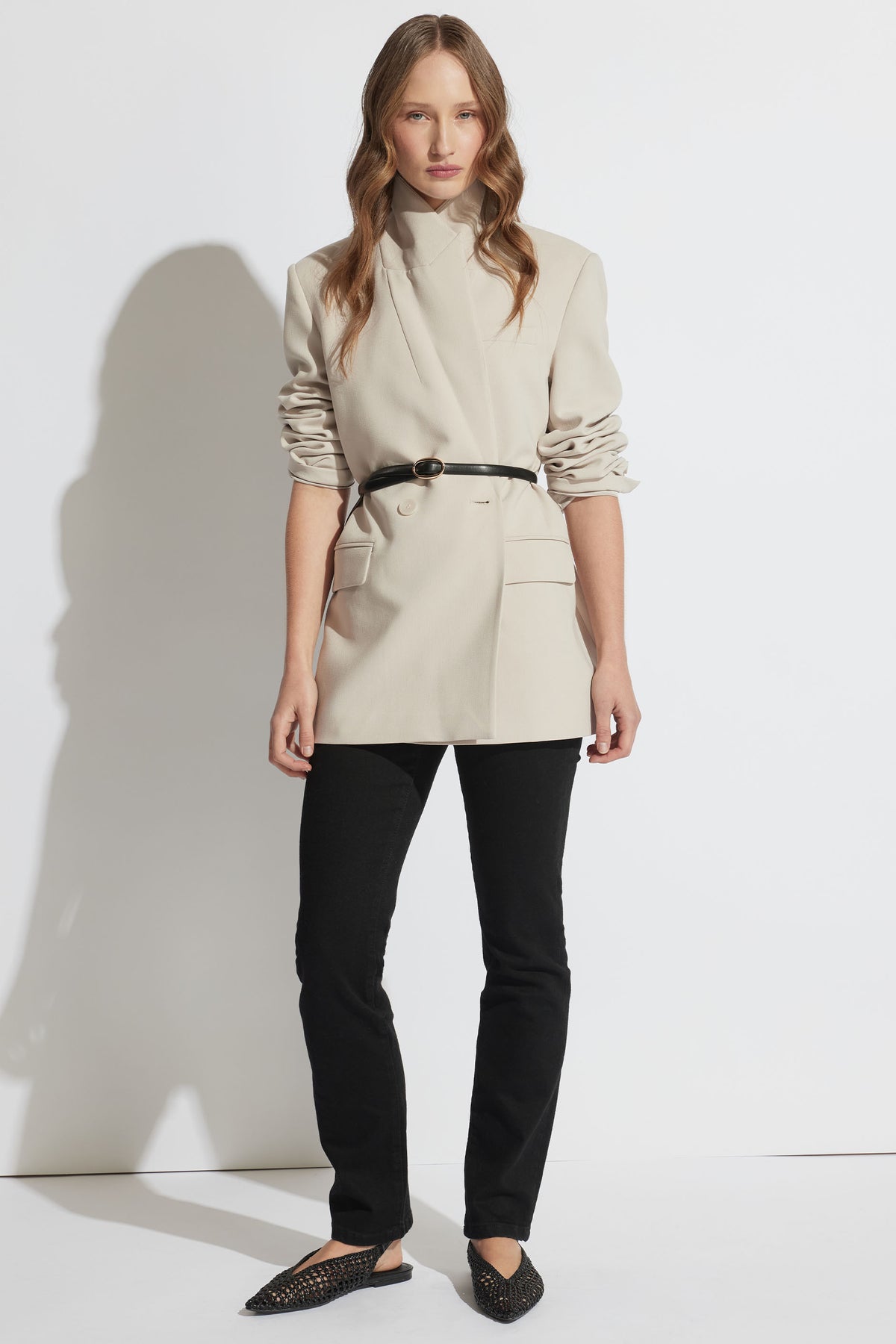 Portrait of a model wearing Billie Straight Leg Jean in black denim paired with a beige blazer and belt, gallery position 1