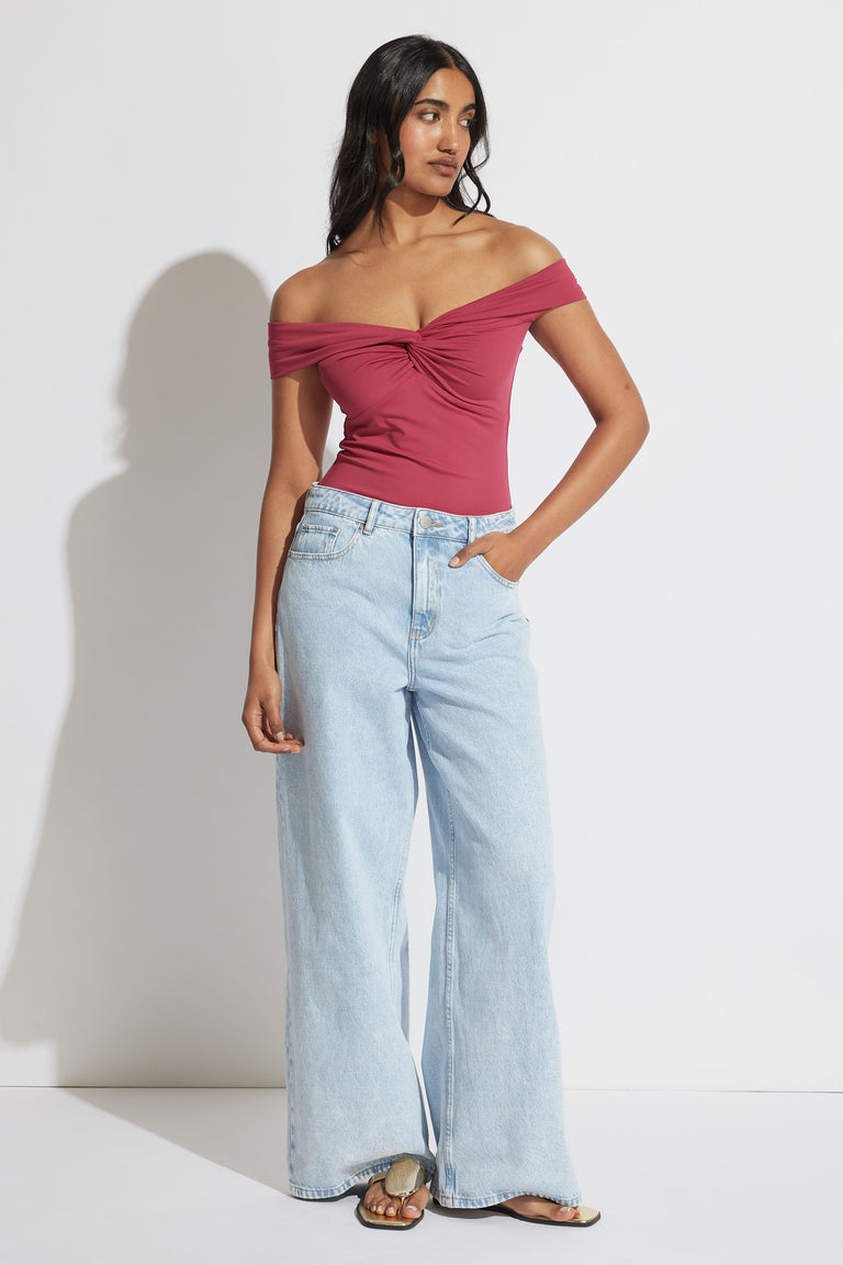 Woman wearing a twisted off-shoulder cerise top paired with light wash wide-leg jeans and slide sandals