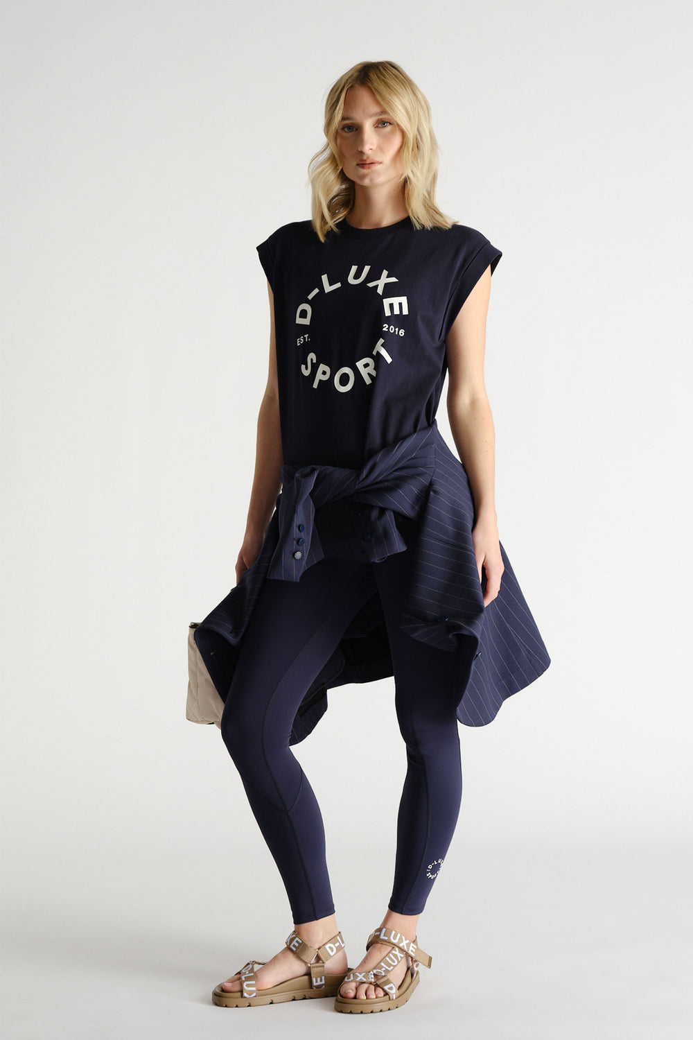 Woman styled in navy graphic tank paired with matching leggings and a pinstriped jacket tied at the waist
